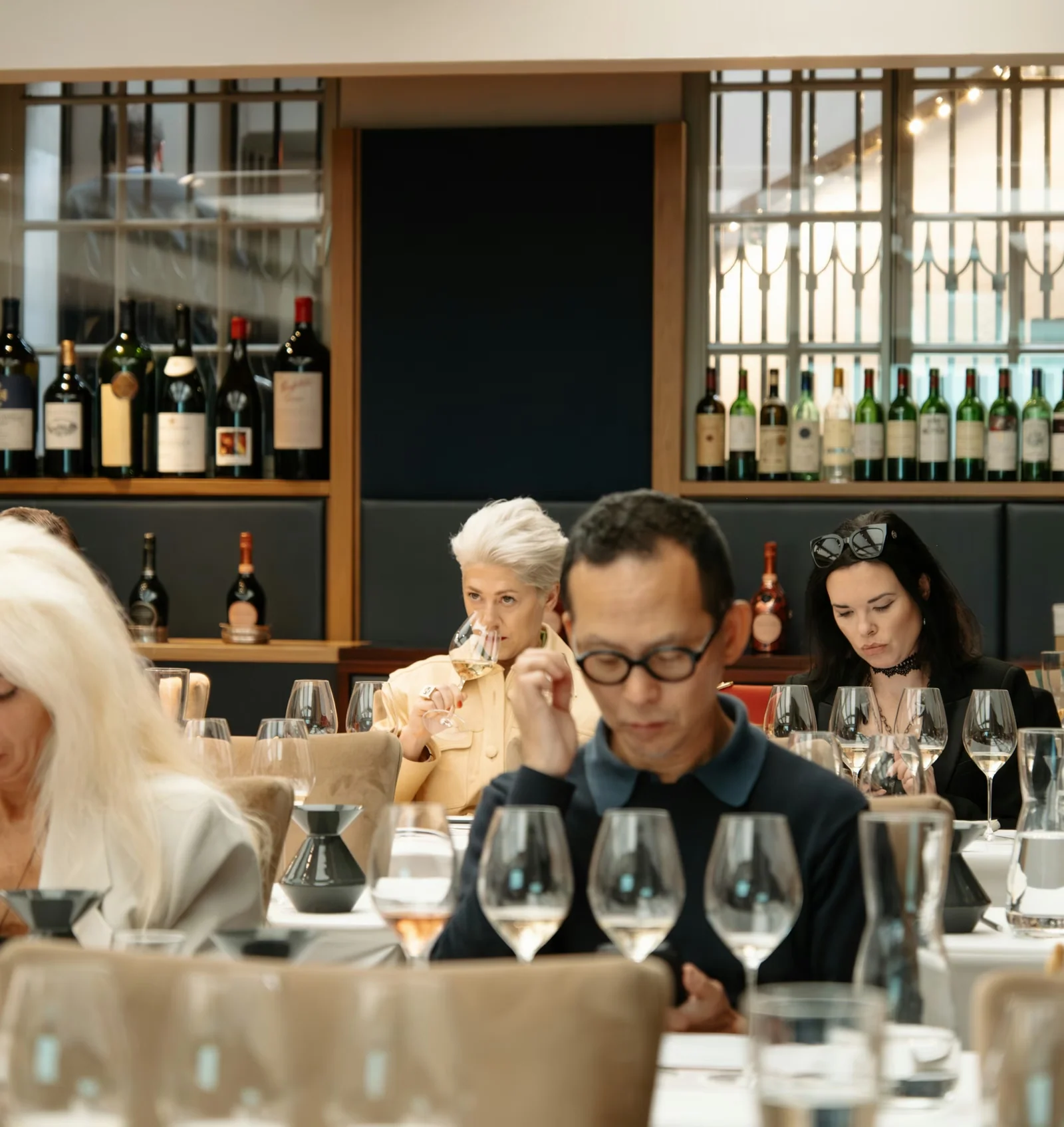 Guests taste wine around a table filled with glasses in a stylish restaurant
