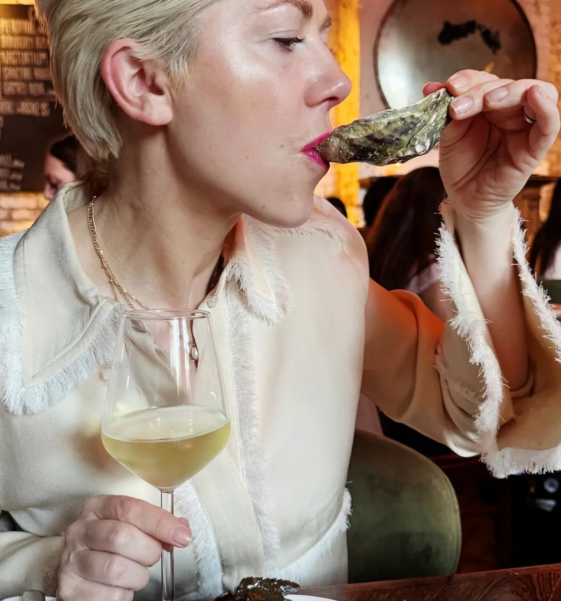 Diner holding an oyster beside a glass of white wine and a bowl of seafood