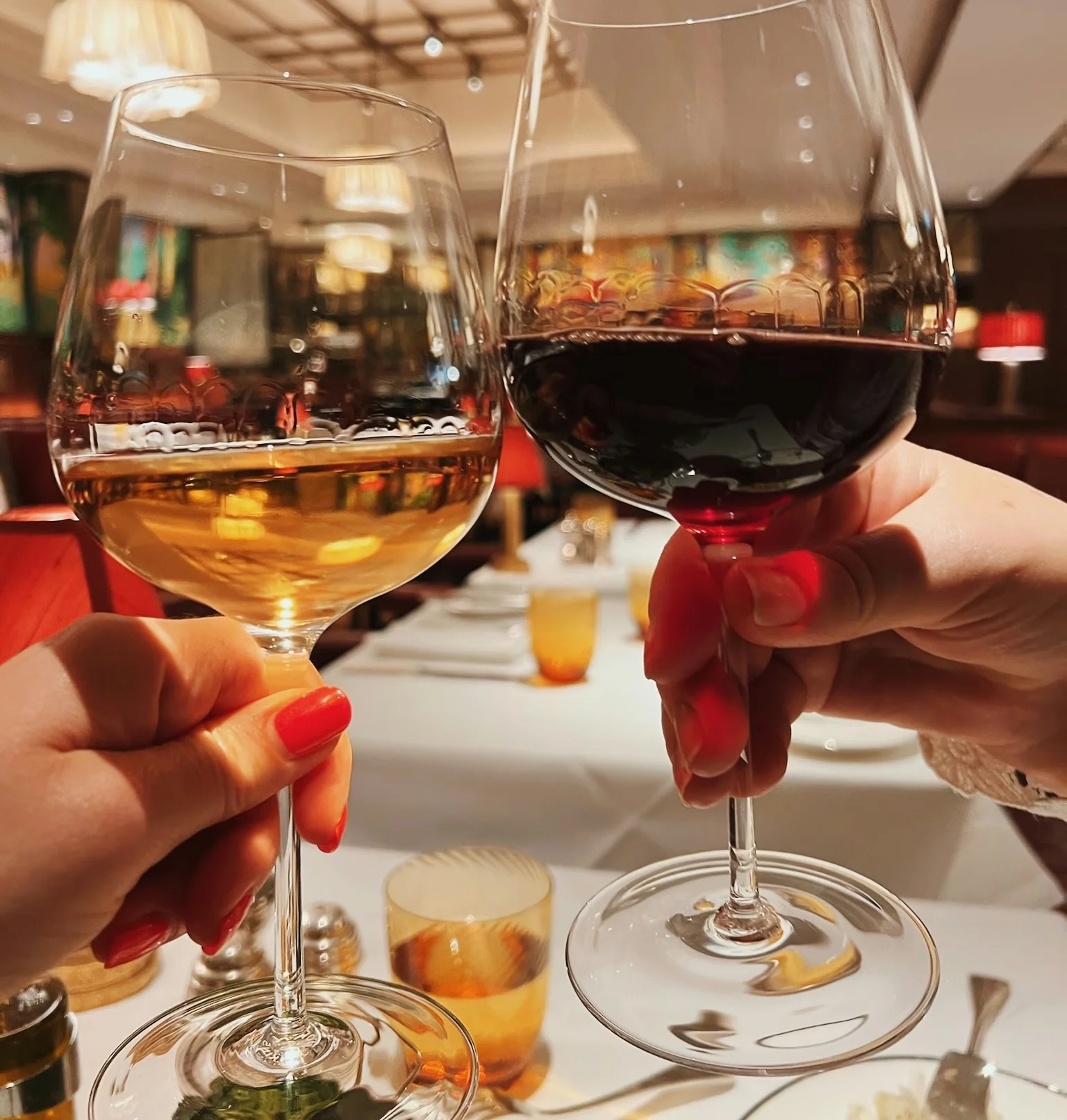 Two hands hold glasses of white and red wine over a restaurant table