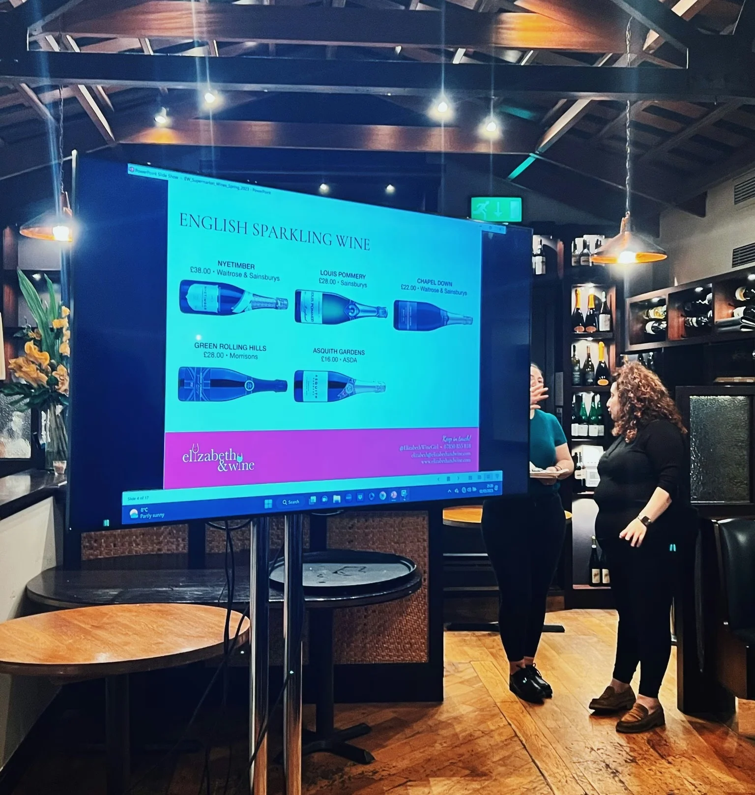 English sparkling wine tasting presentation on a screen in a bar, with two people standing beside it