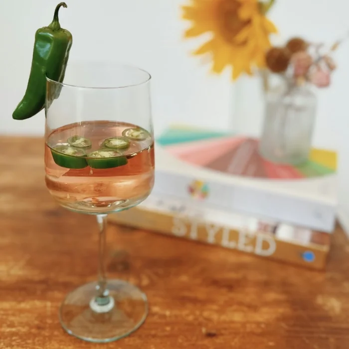 Wine glass with jalapeño garnish and pink cocktail on wooden table