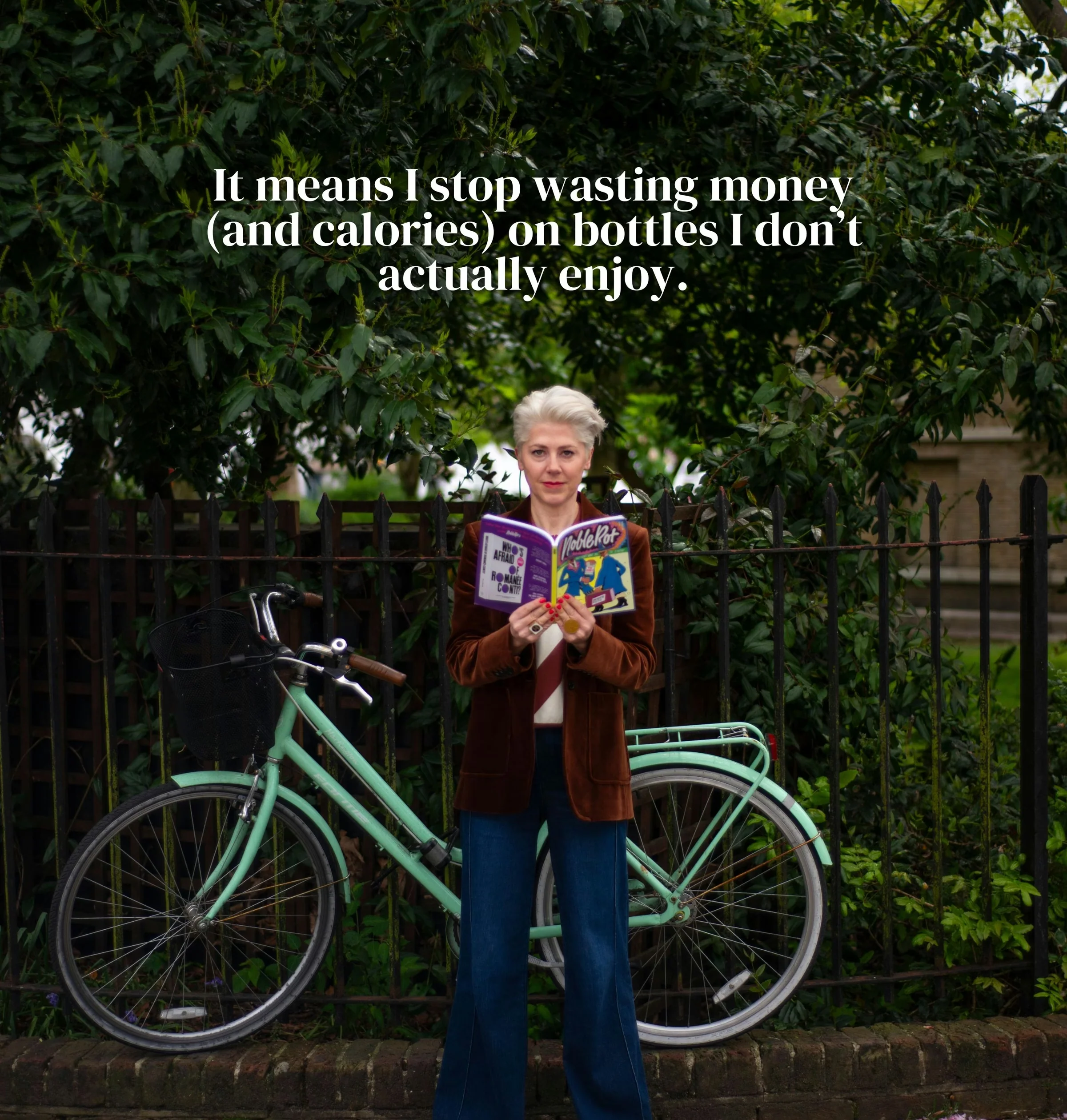 Person holding an open comic book beside a mint-green bicycle under leafy trees