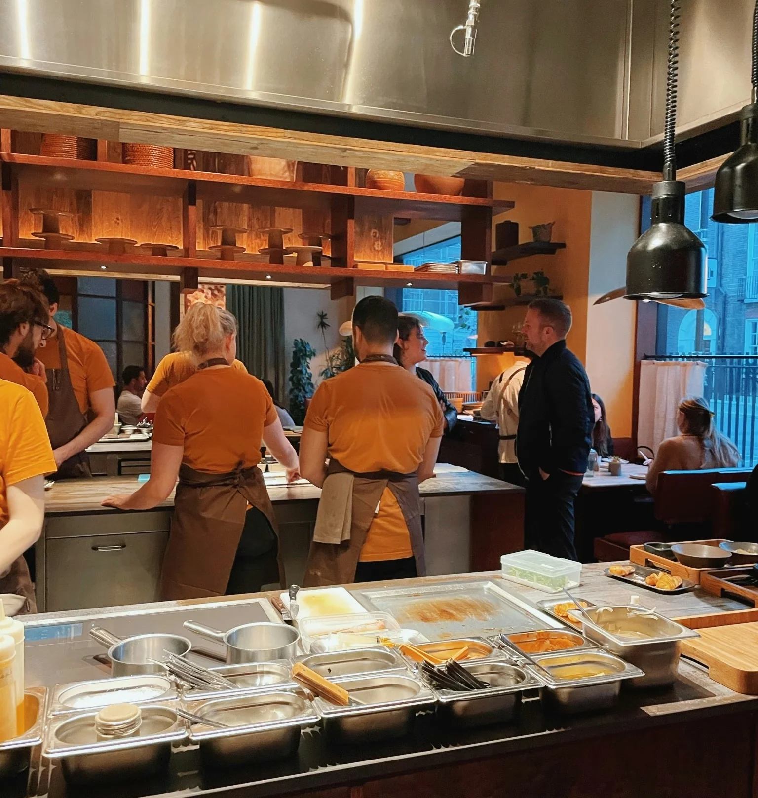 Restaurant kitchen with chefs preparing food and diners seated beside the counter
