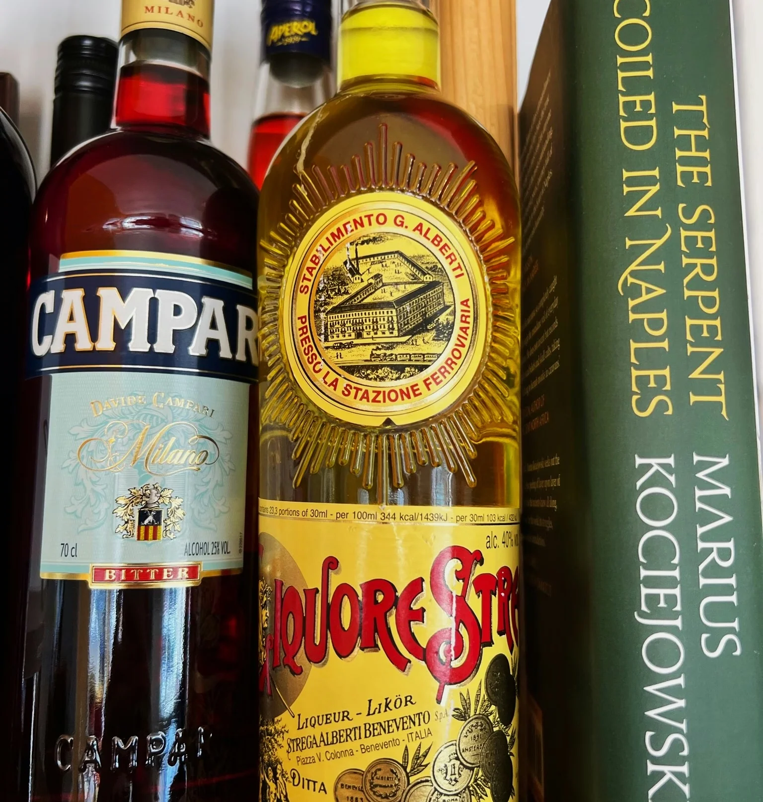 Close-up of Campari, Aperol and Liquore Strega bottles beside a book about Italian cocktails