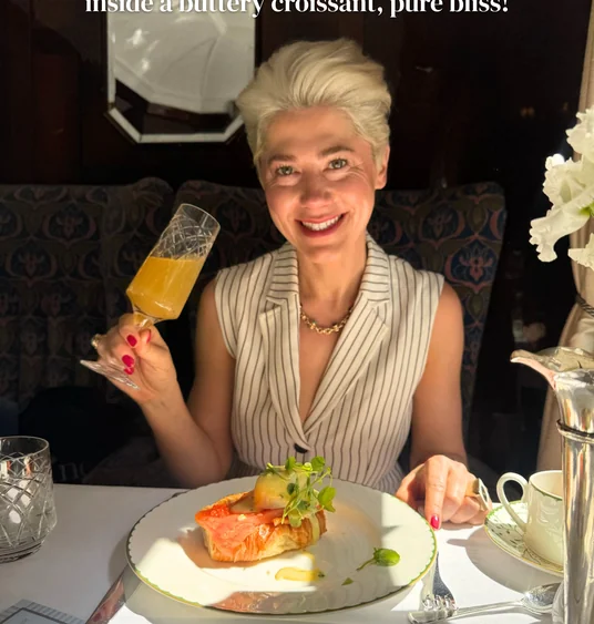 Diner raising a glass beside a plated smoked fish dish aboard a luxury train