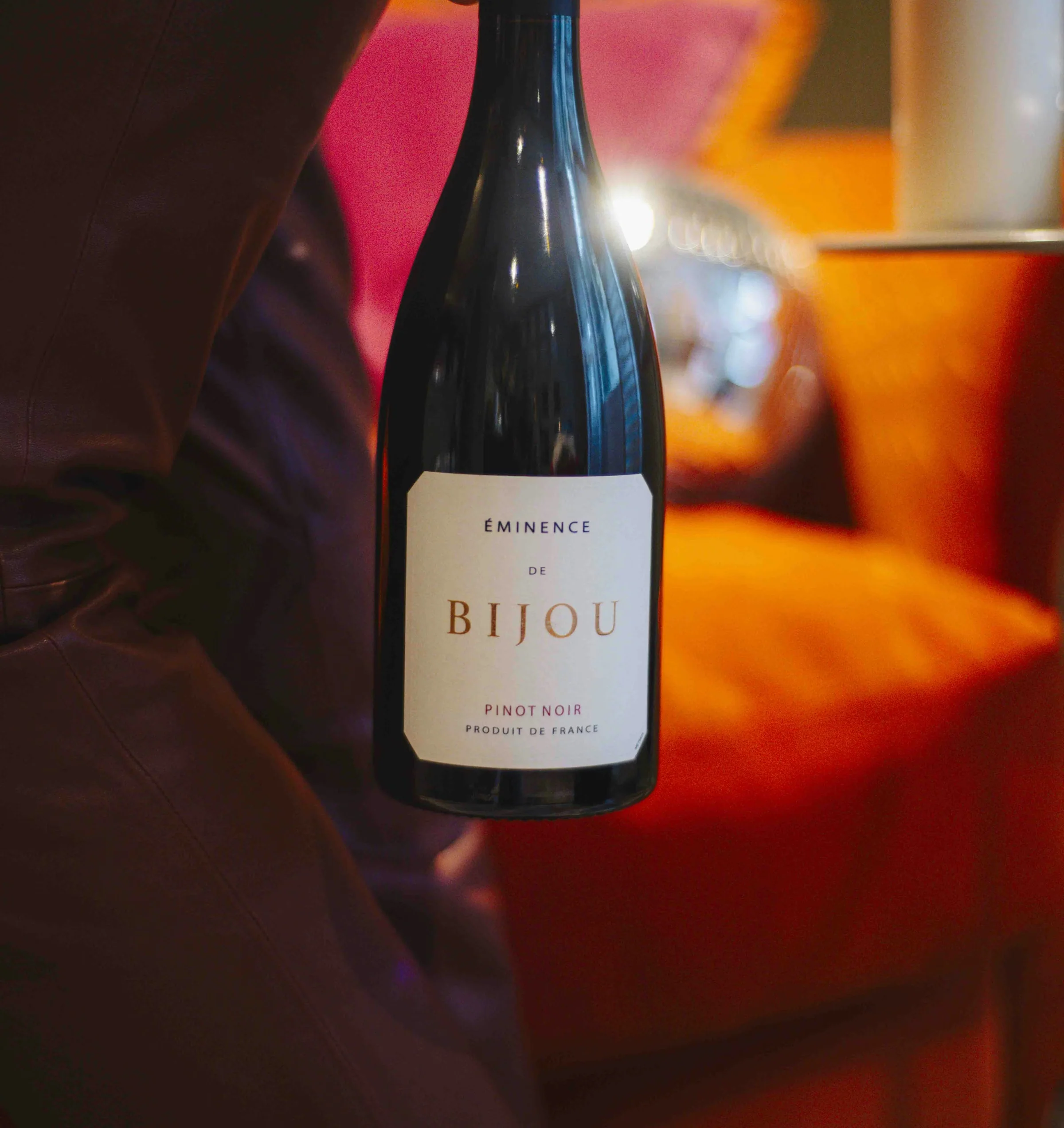 Hand holding a bottle of Bijou Pinot Noir beside a lit candle