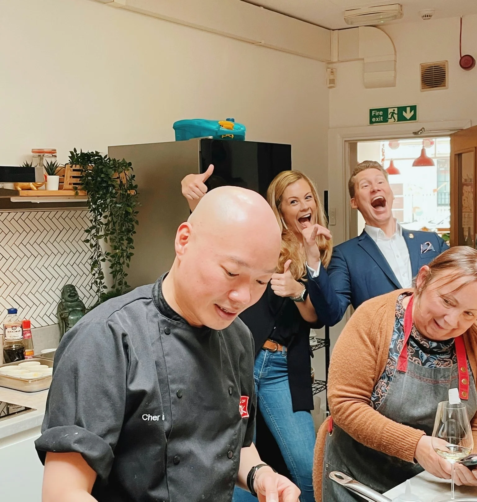 Chef and guests laughing in a kitchen during a wine tasting