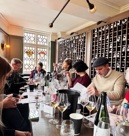 Guests taste wine around a table in a private dining room with stained-glass windows and wine storage walls