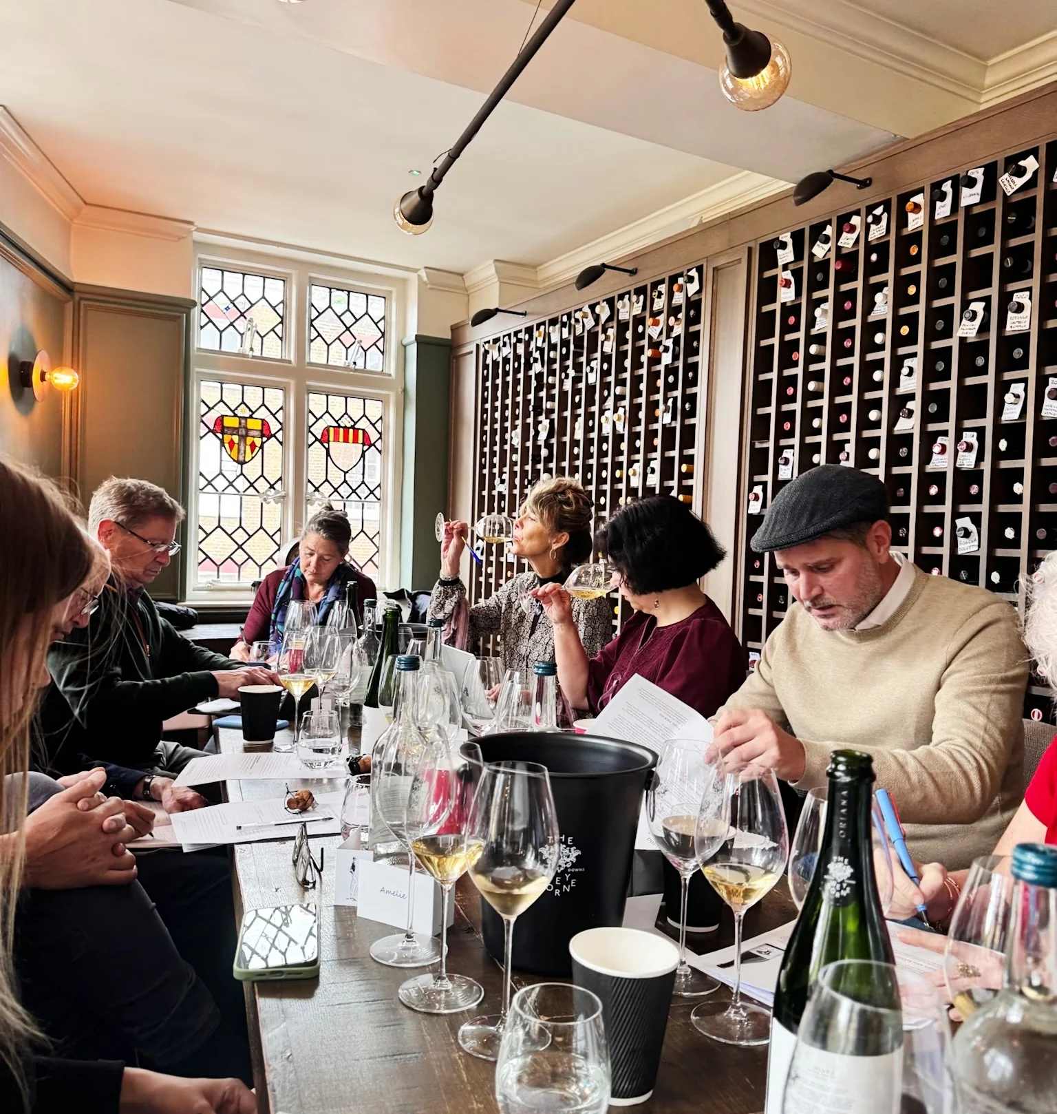 Guests taste wine around a table in a private dining room with stained-glass windows and wine storage walls