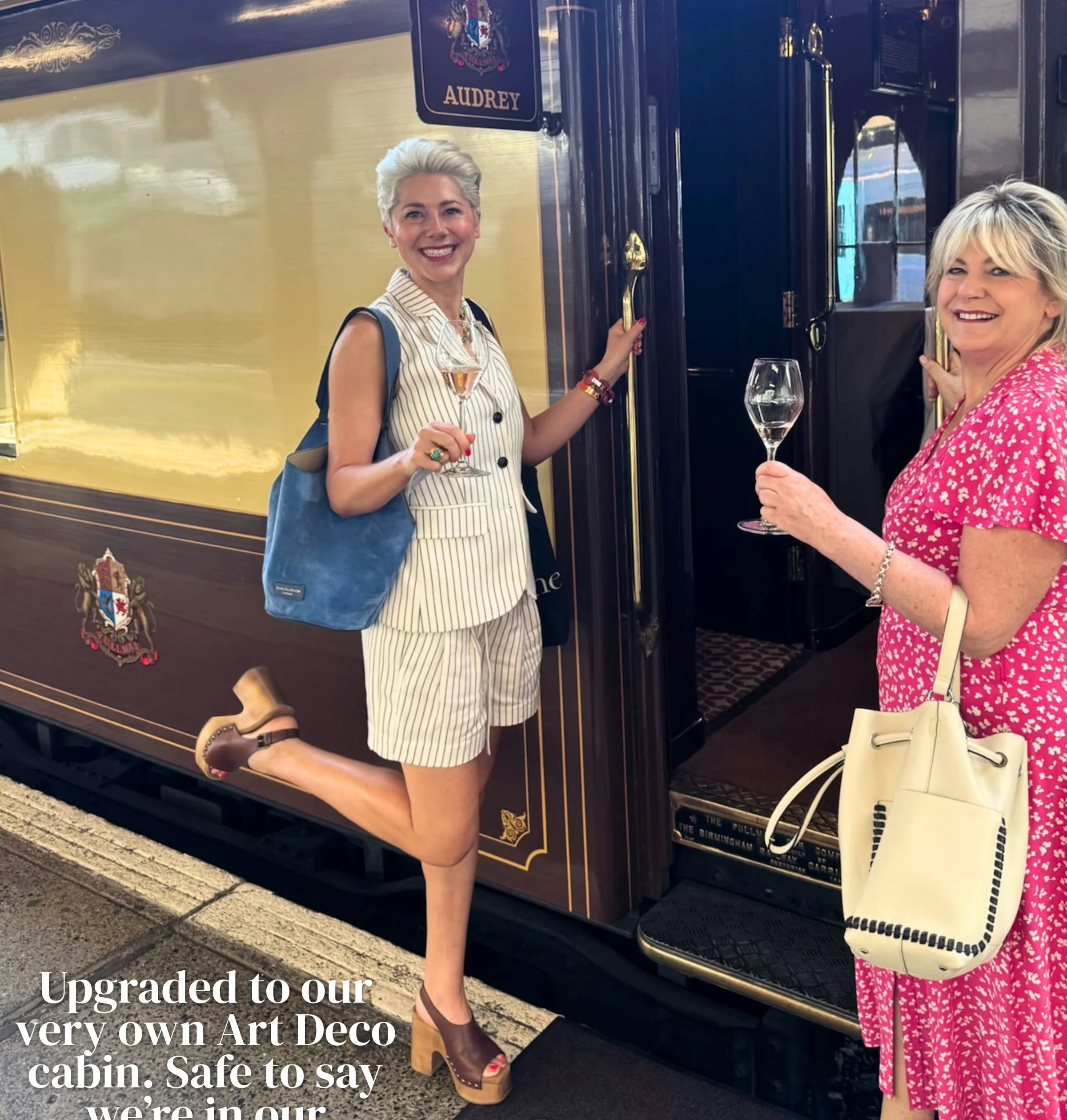 Two women holding wine glasses beside the Audrey carriage on the British Pullman
