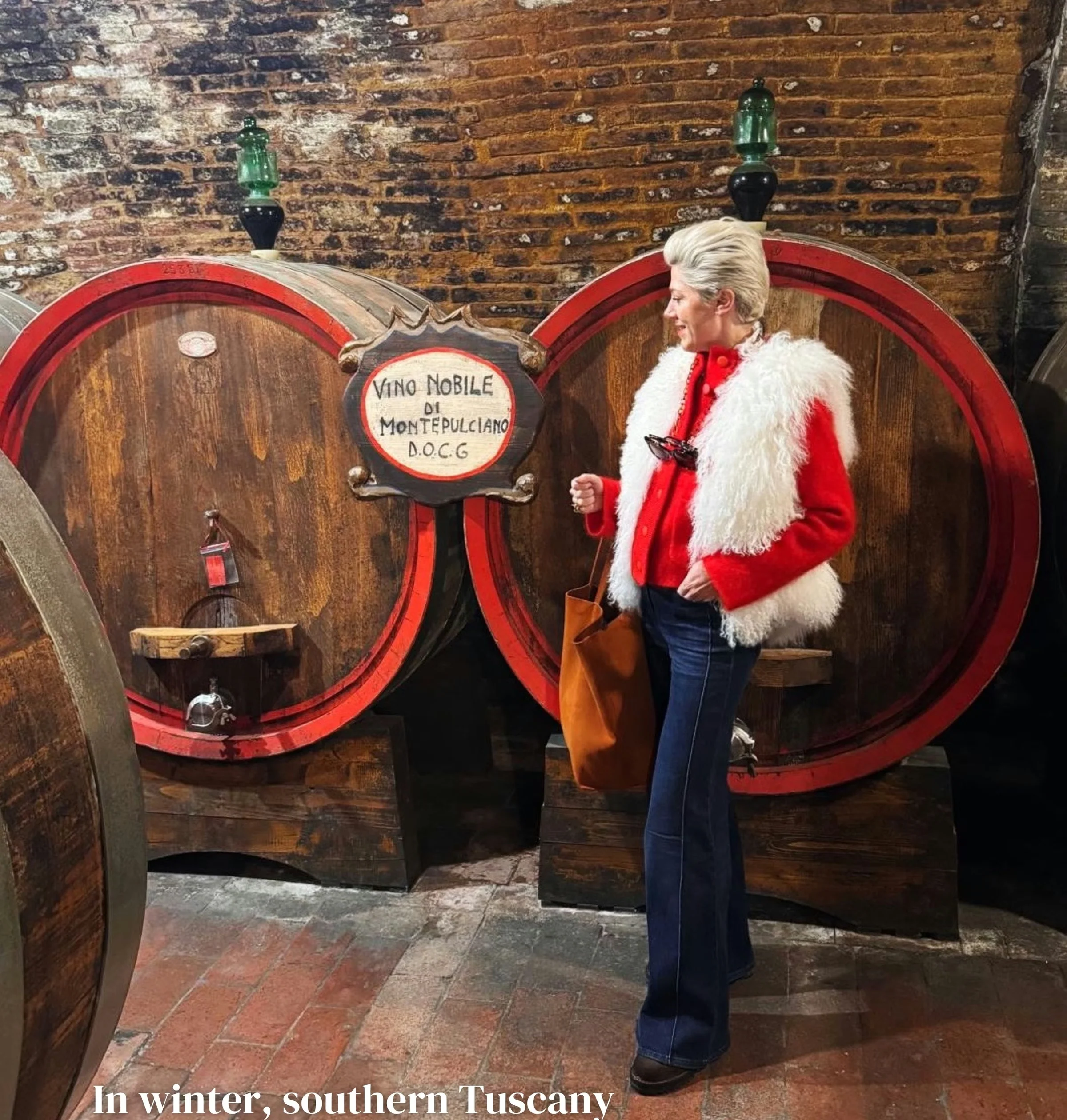 Woman in a red jacket standing beside large wine barrels in a Tuscan cellar
