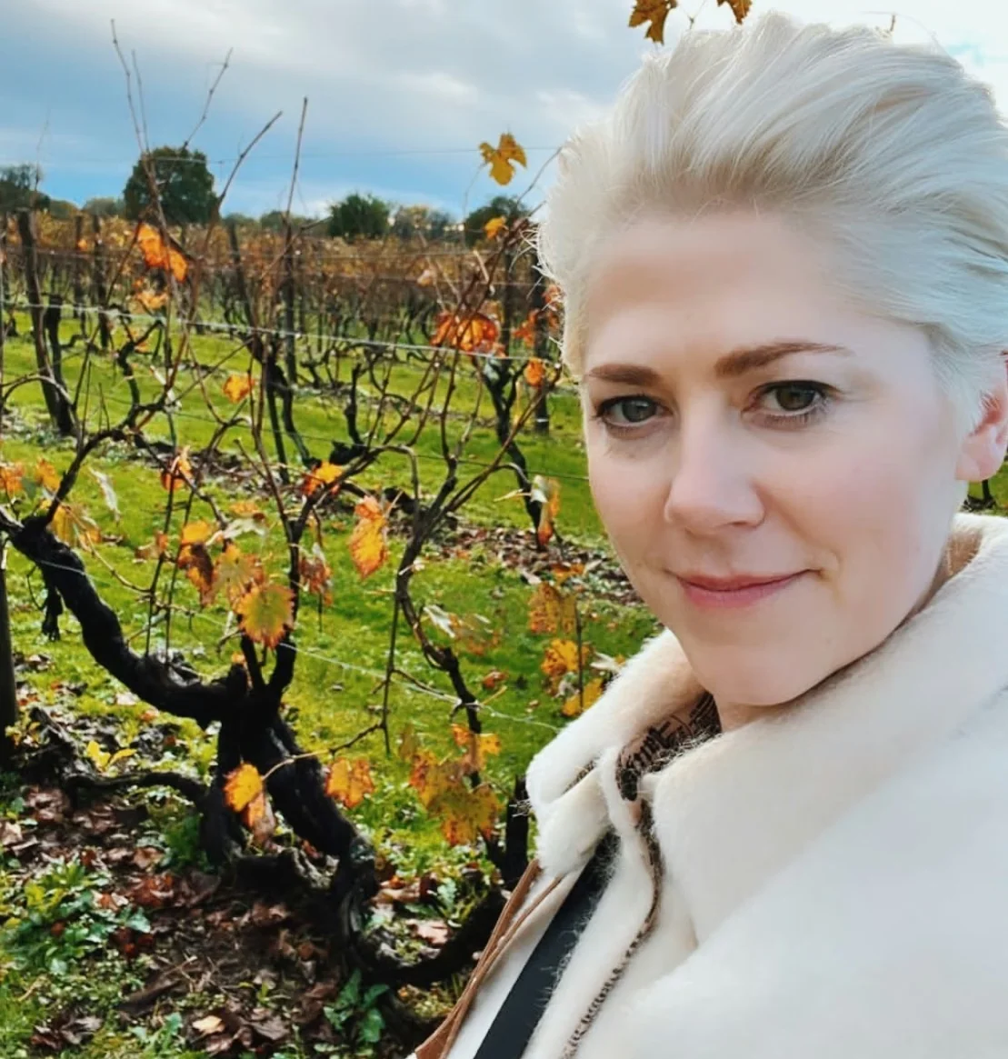 Elizabeth Hawthornthwaite poses beside old vines with autumn leaves in an Italian vineyard