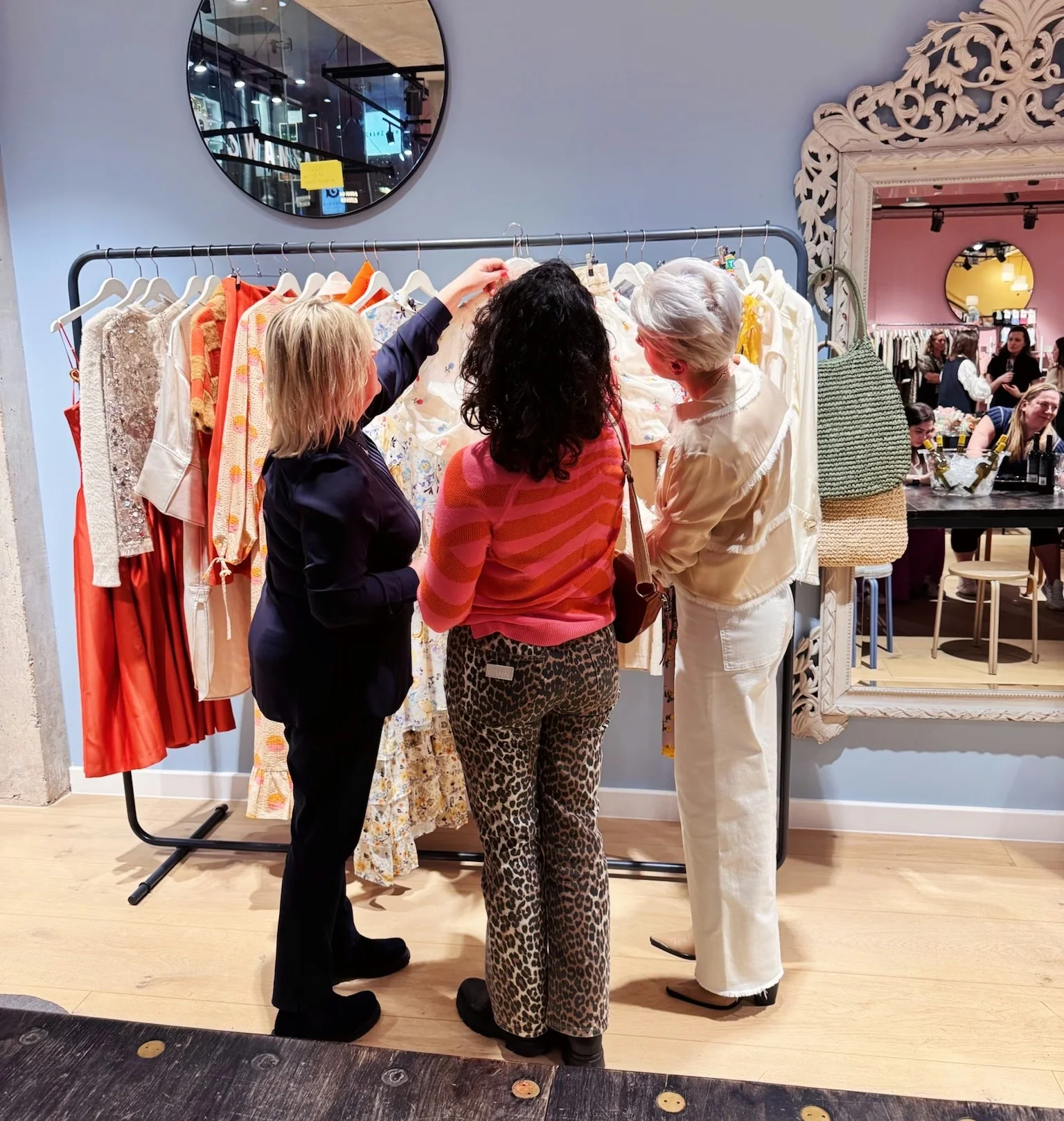 Three women browse colourful clothing on a rail in a stylish shop