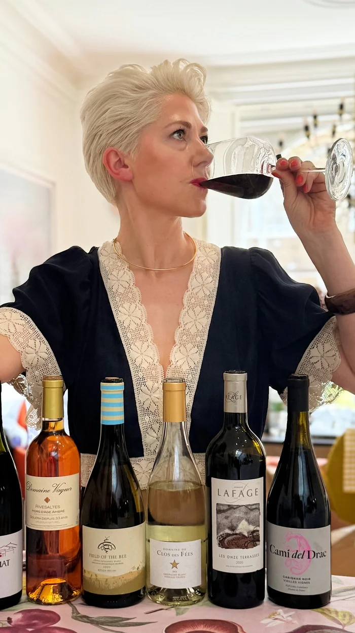 Woman tasting red wine beside five bottles at a table