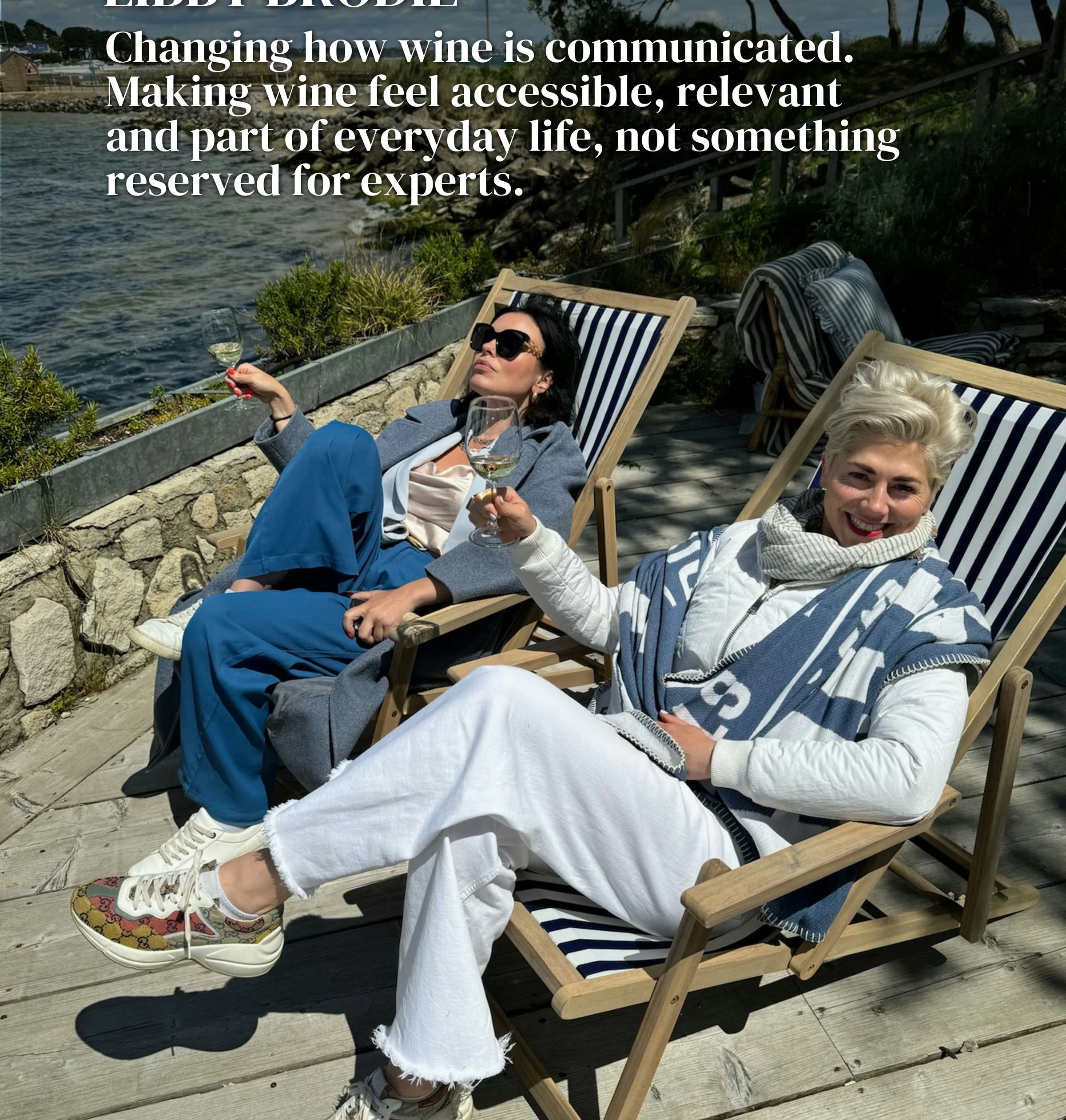 Two women relaxing in deckchairs by the water with glasses of wine