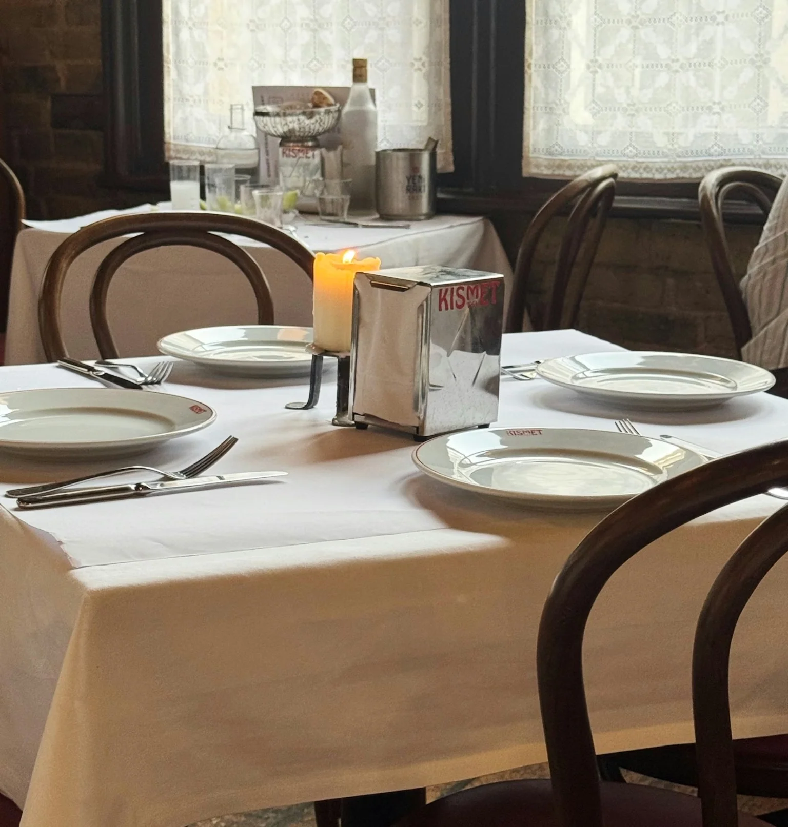 Candlelit restaurant table set with white plates, cutlery and a Kismet table sign