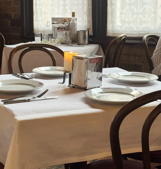 Candlelit restaurant table set with white plates, cutlery and a Kismet table sign