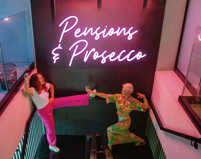 Two women posing with wine glasses beneath Pensions & Prosecco sign