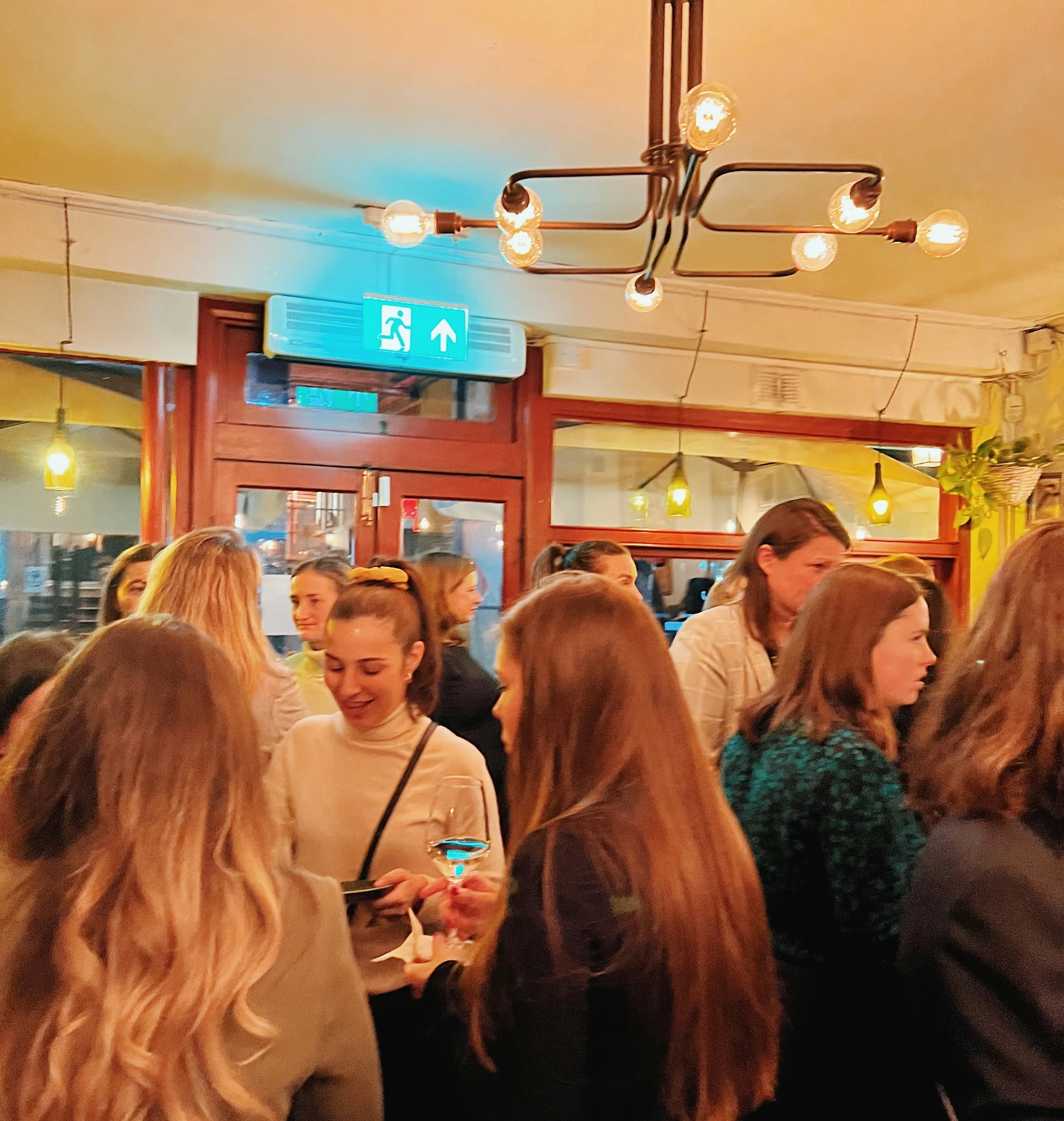 Guests mingle at a busy indoor wine event beneath warm pendant lights