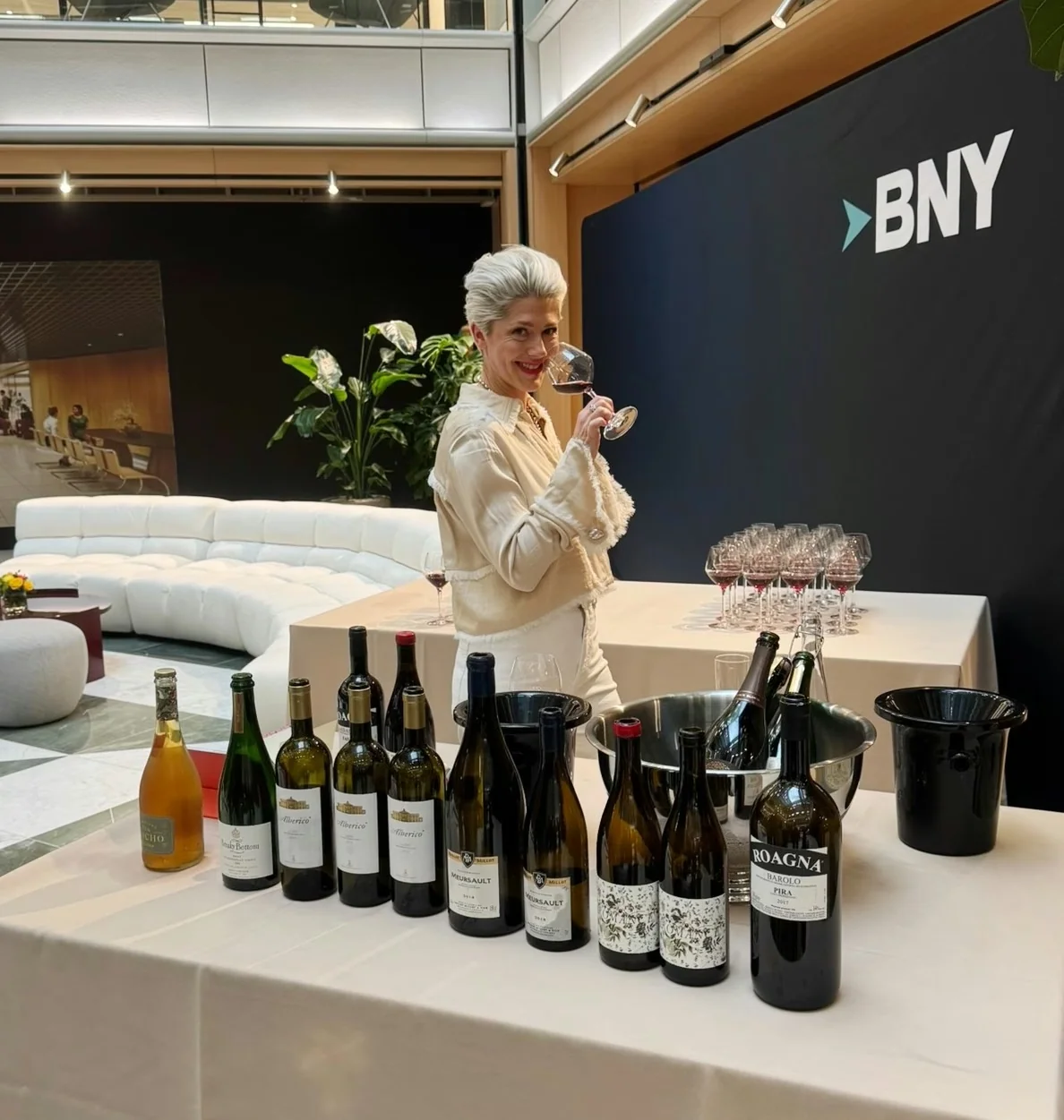 Elizabeth Hawthornthwaite pours wine at a tasting table in a London office displaying BNY branding