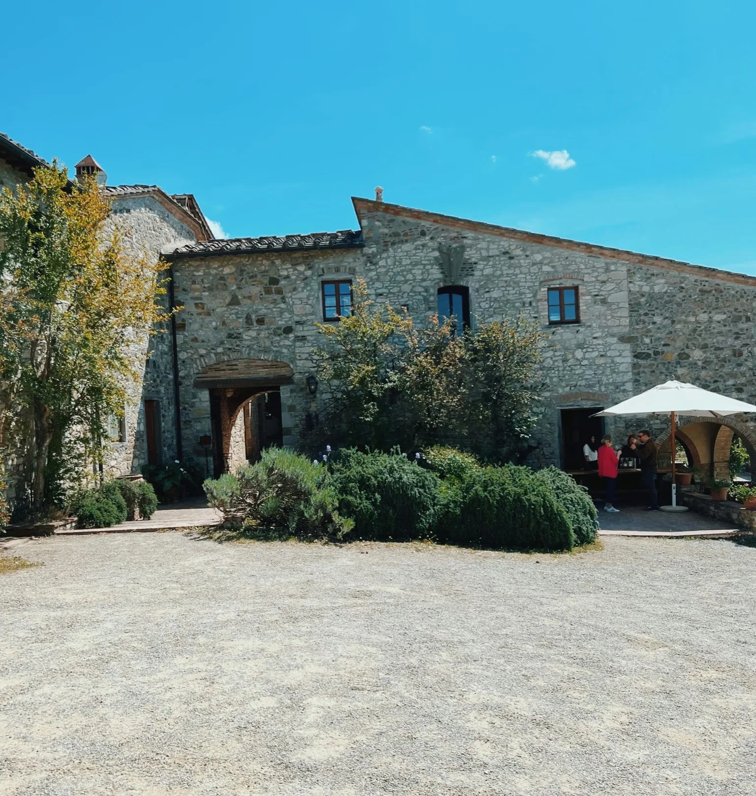 Stone buildings at Fontodi Winery in Tuscany, with shrubs, an umbrella and people outside