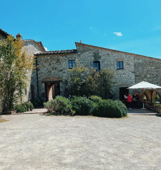 Stone buildings at Fontodi Winery in Tuscany, with shrubs, an umbrella and people outside