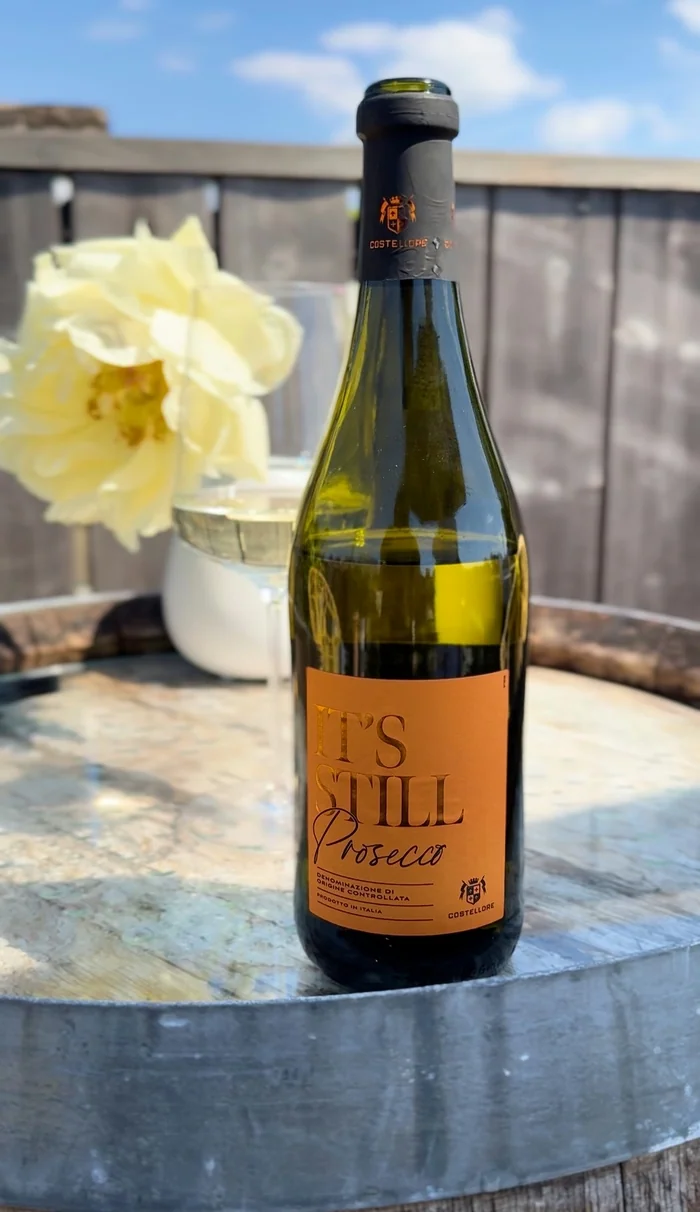 Prosecco bottle with glass and pale flower on wooden table