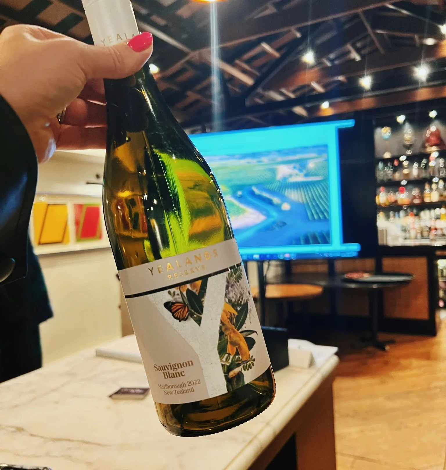 Hand holding a Yealands Reserve Sauvignon Blanc bottle in a stylish bar