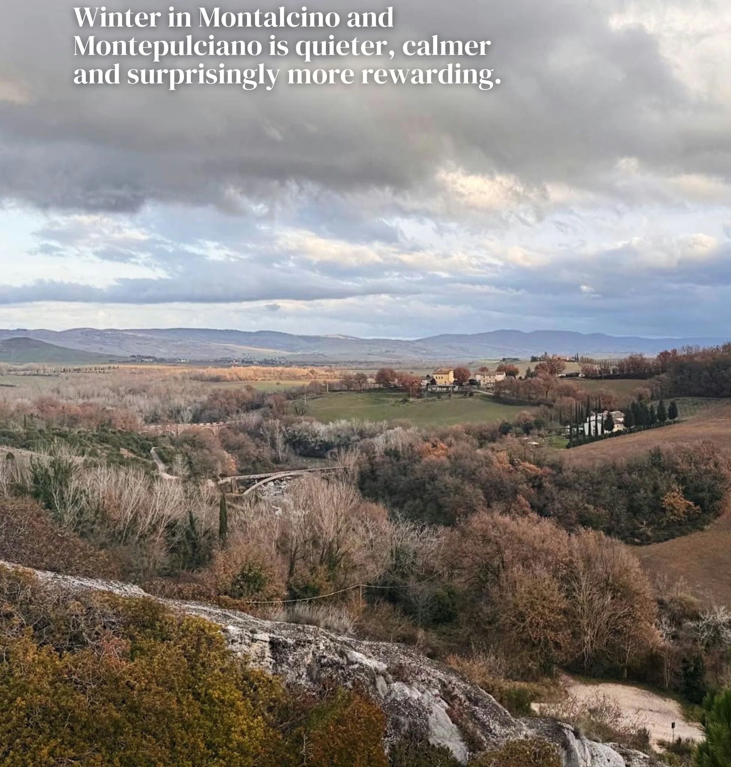 Winter landscape of rolling Tuscan hills, fields and a rural village beneath dramatic clouds