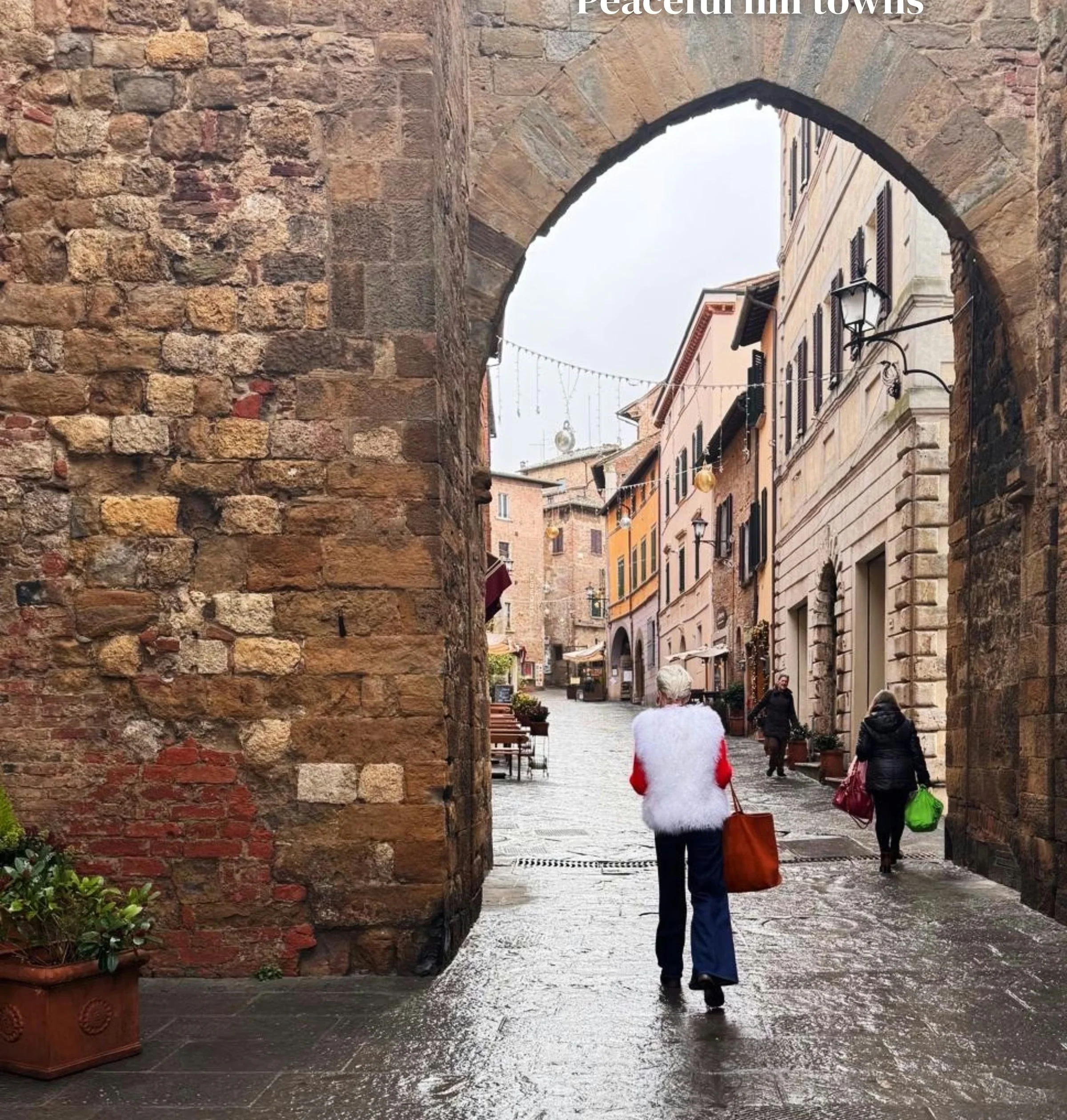 Rainy Tuscan hill town street viewed through a historic stone arch