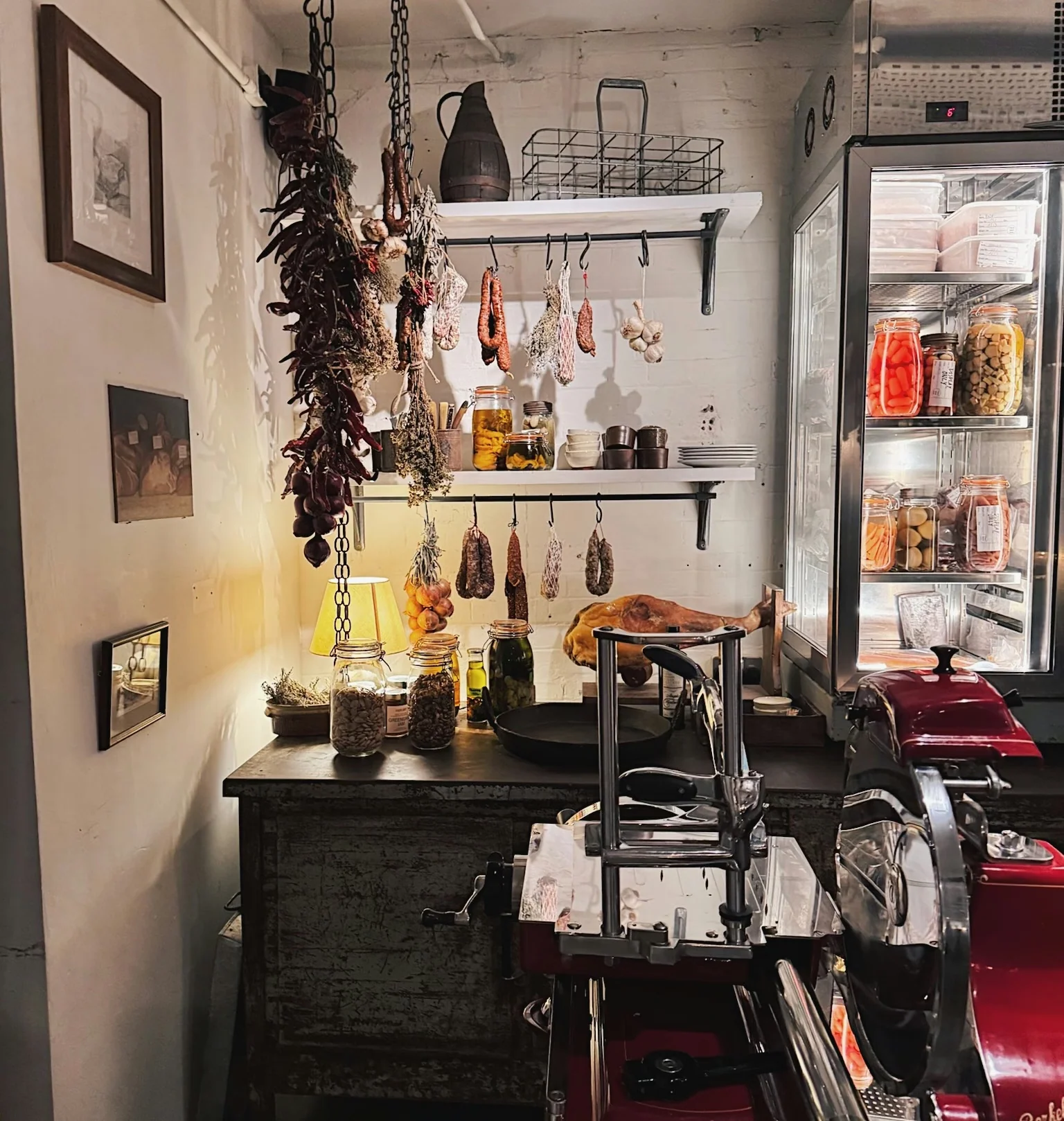Farm shop interior with hanging cured meats, jars of preserves and a red Berkel slicer