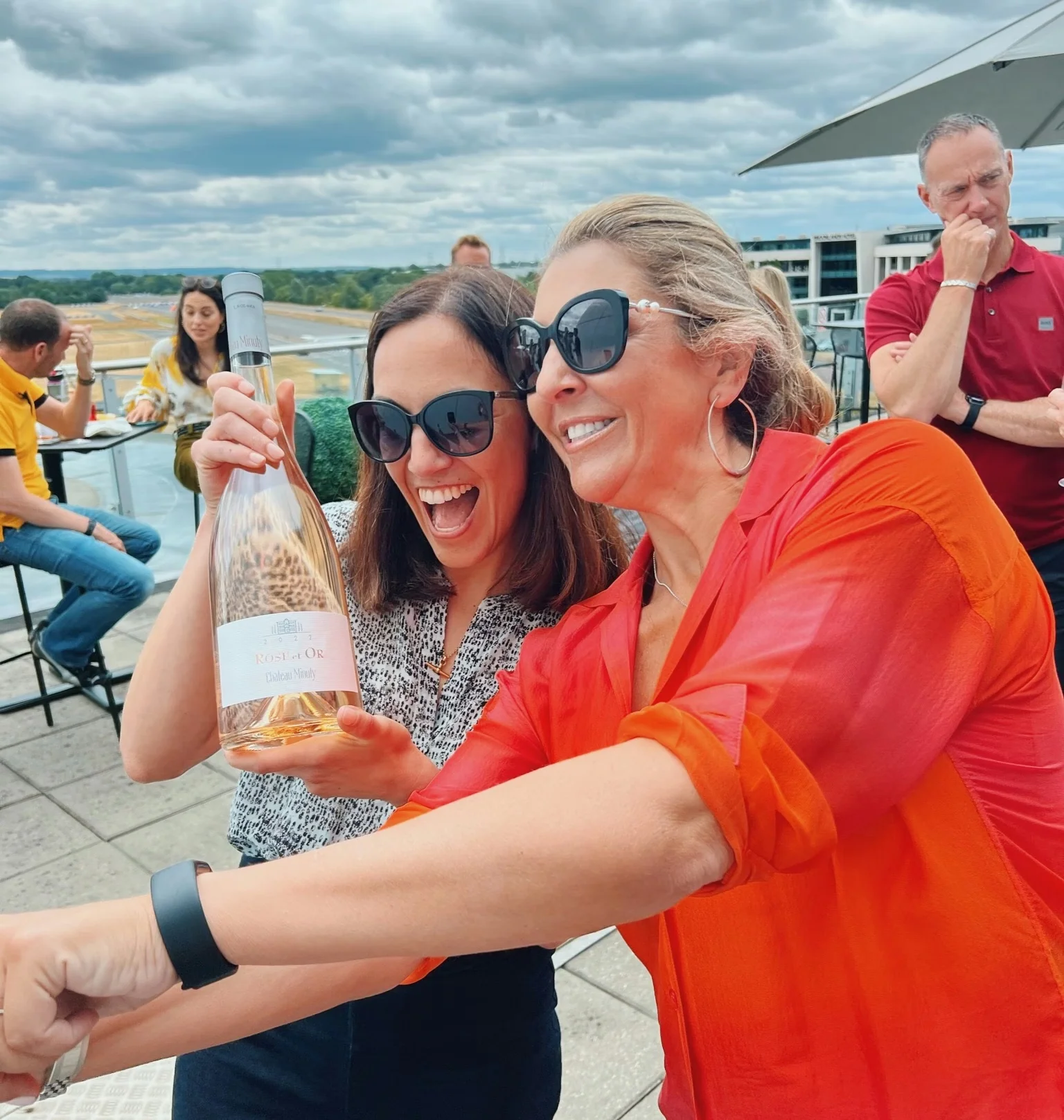 Two women smiling on a terrace while holding a bottle of Rosé d'Or wine