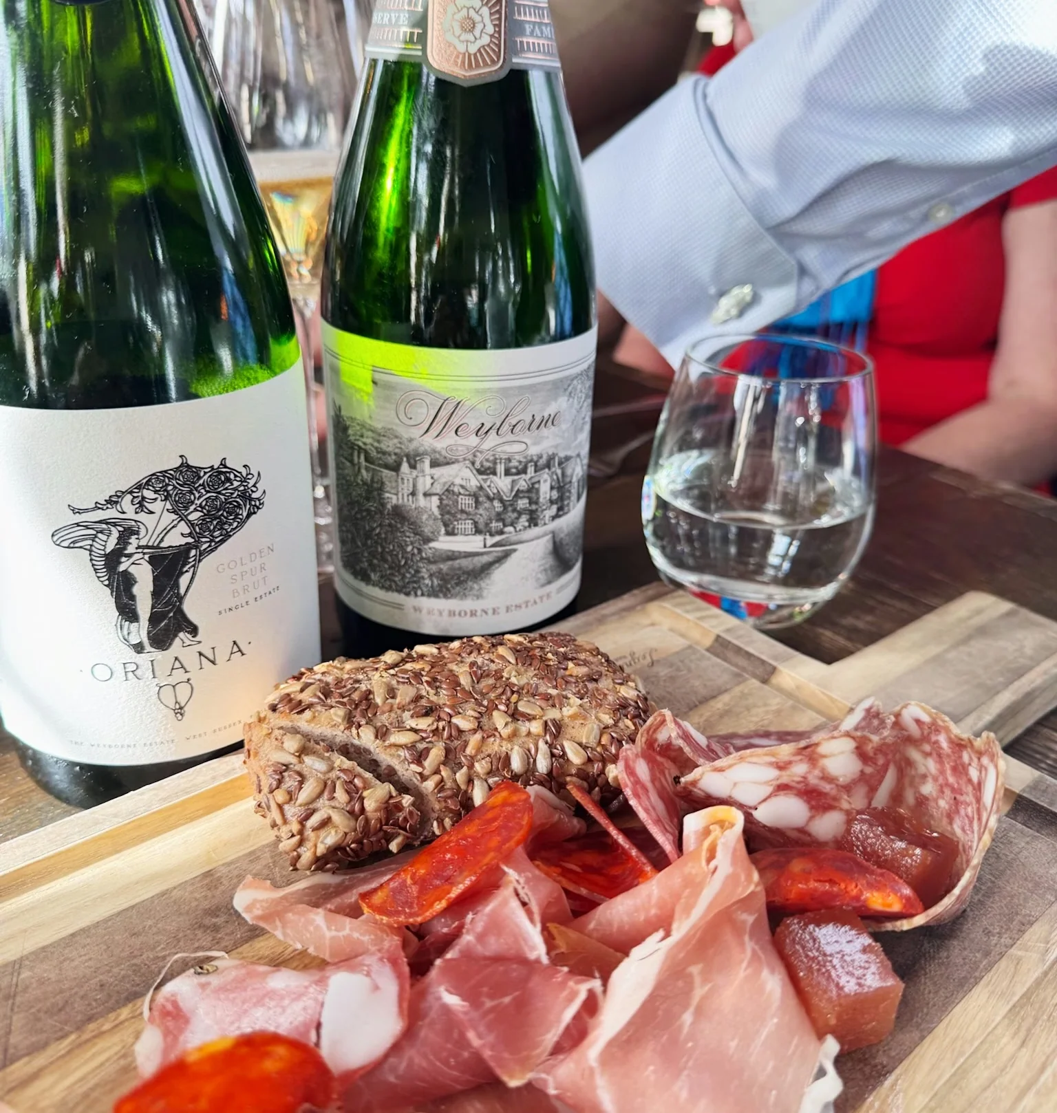 English sparkling wine bottles, a filled glass and charcuterie board on a table
