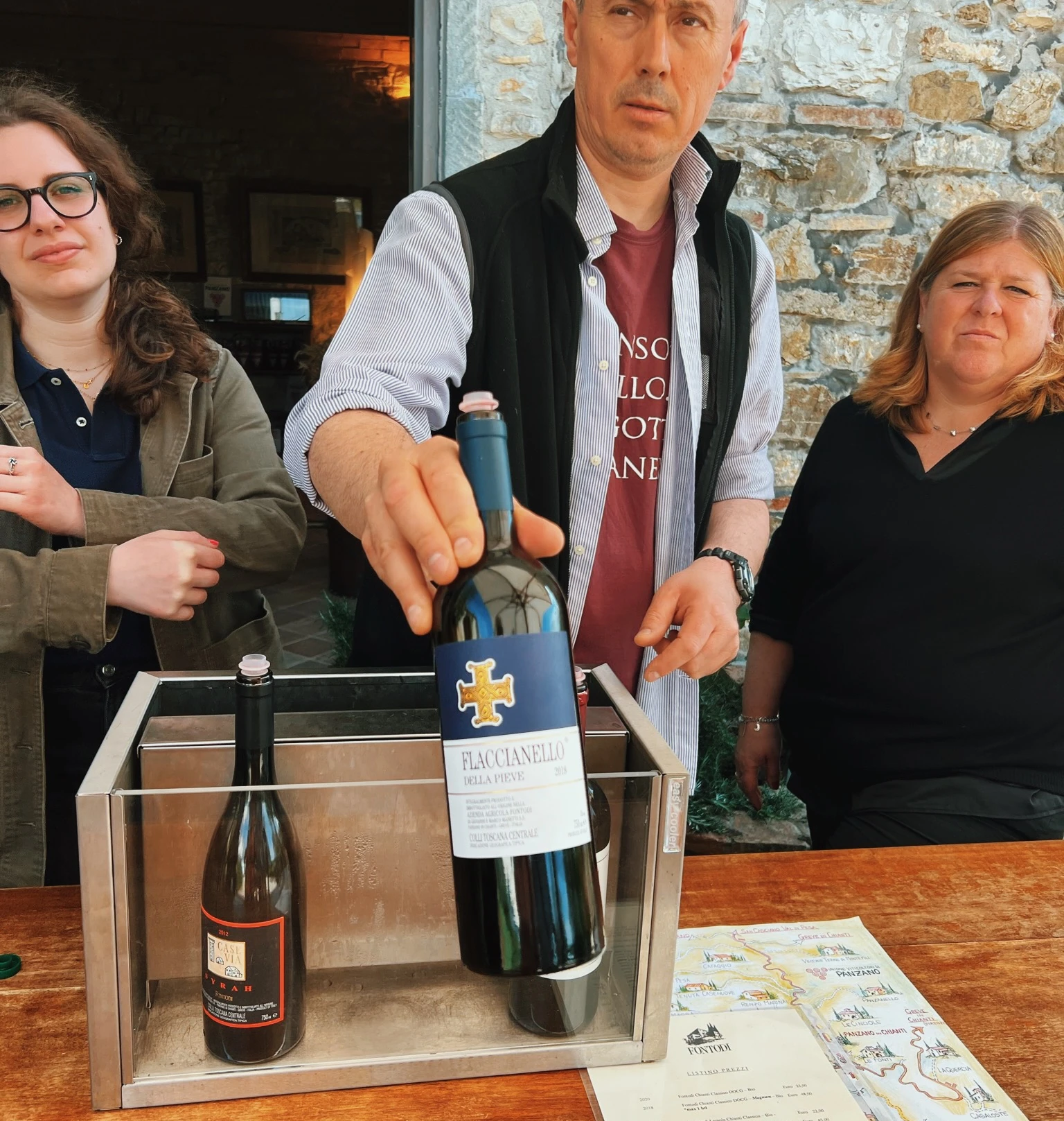 Three people present Italian wine at a winery, with a bottle of Flaccianello held above two displayed bottles