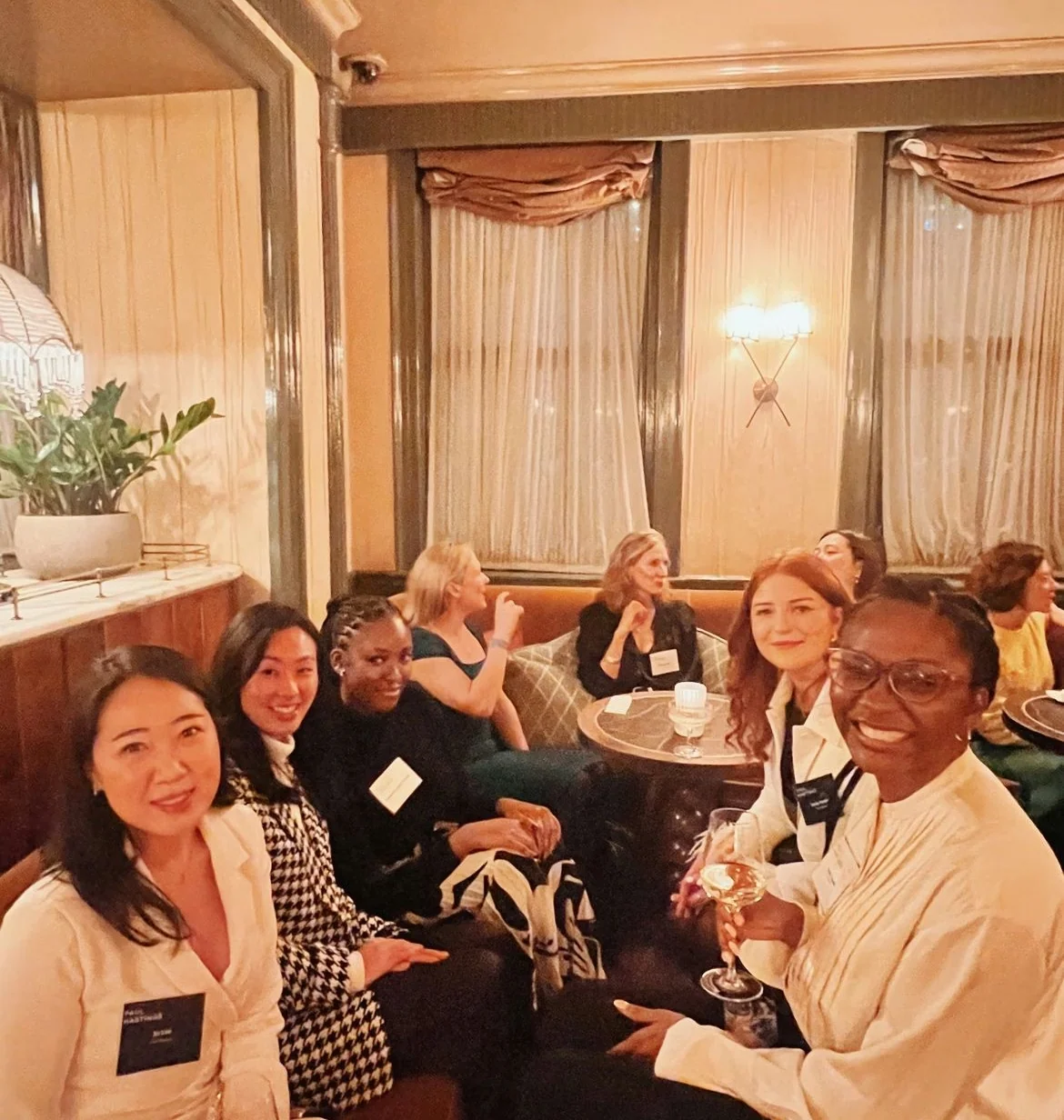 Women sit together with glasses of wine at a warmly lit event in Kettner’s Champagne Bar