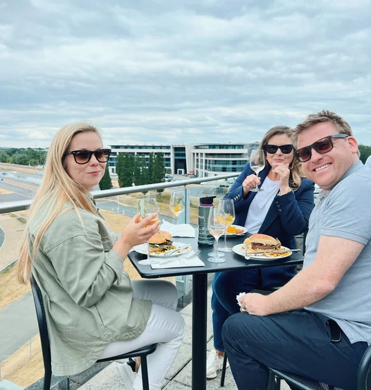 Three people enjoy wine and burgers on a terrace overlooking Mercedes-Benz World