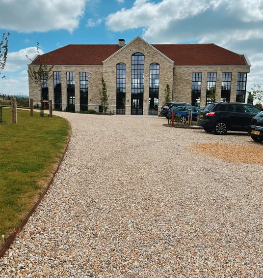 Exton Park’s stone winery building with red roof, gravel drive, parked cars and blue sky