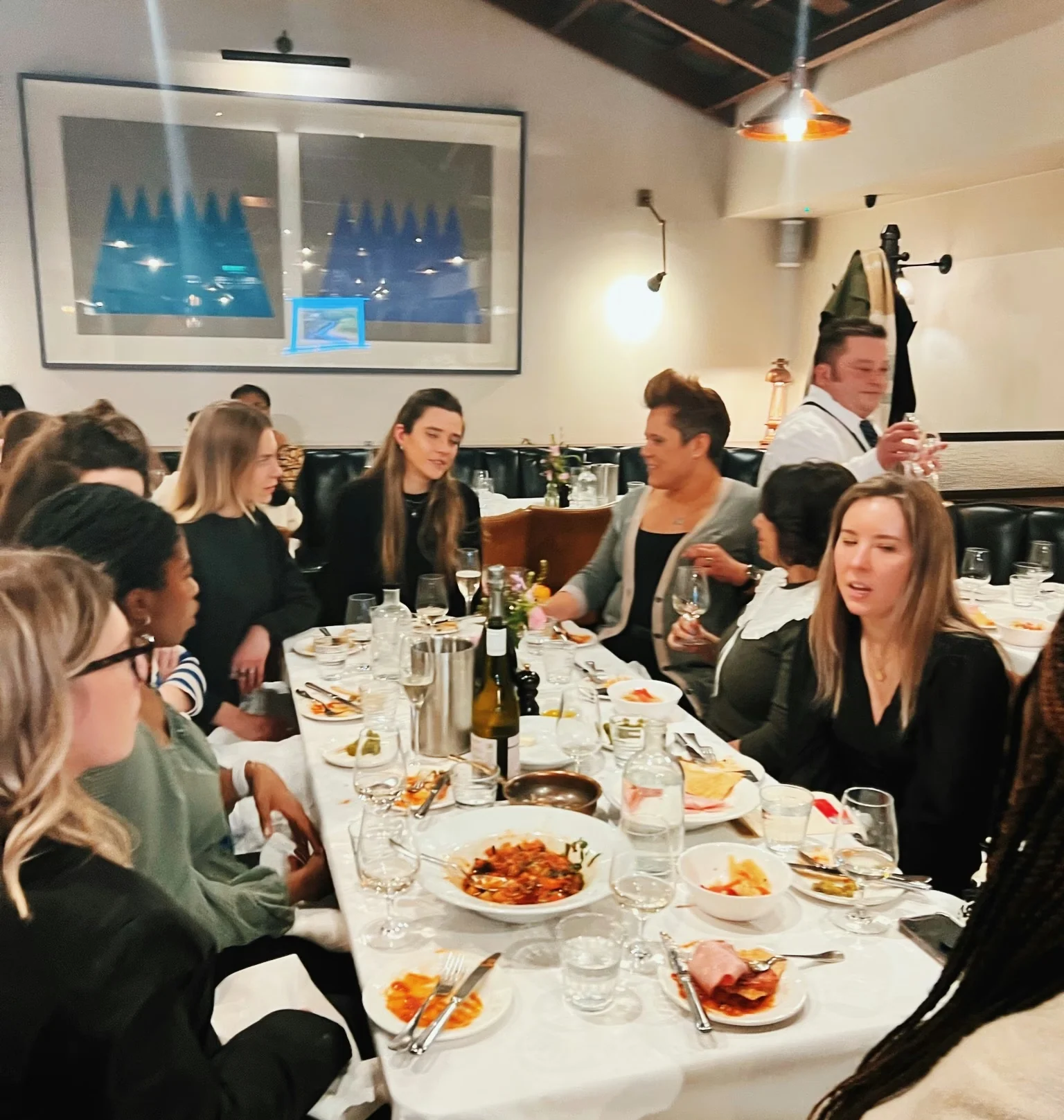 Guests gathered around a restaurant table with wine glasses, plates of food and a bottle