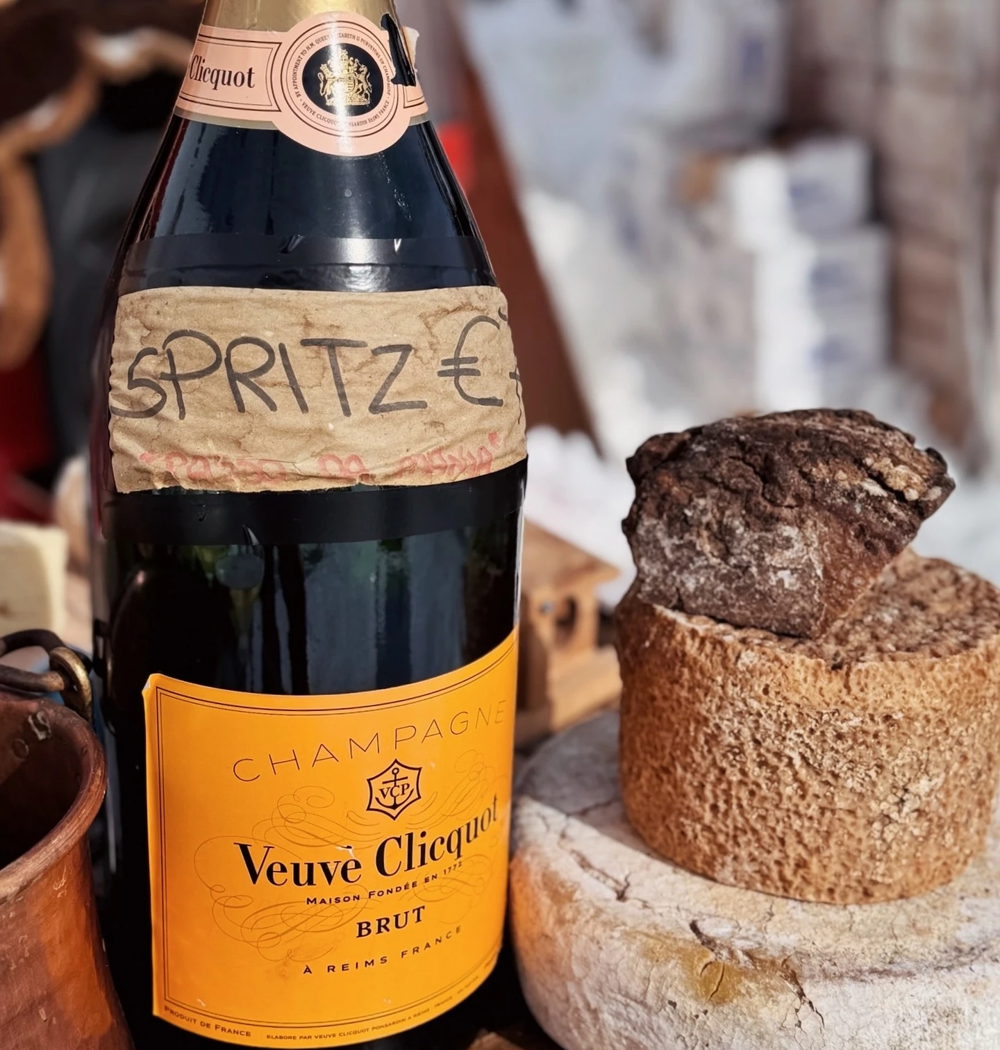 Veuve Clicquot champagne bottle labelled ‘SPRITZ’ beside stacked loaves of bread on a wooden bar