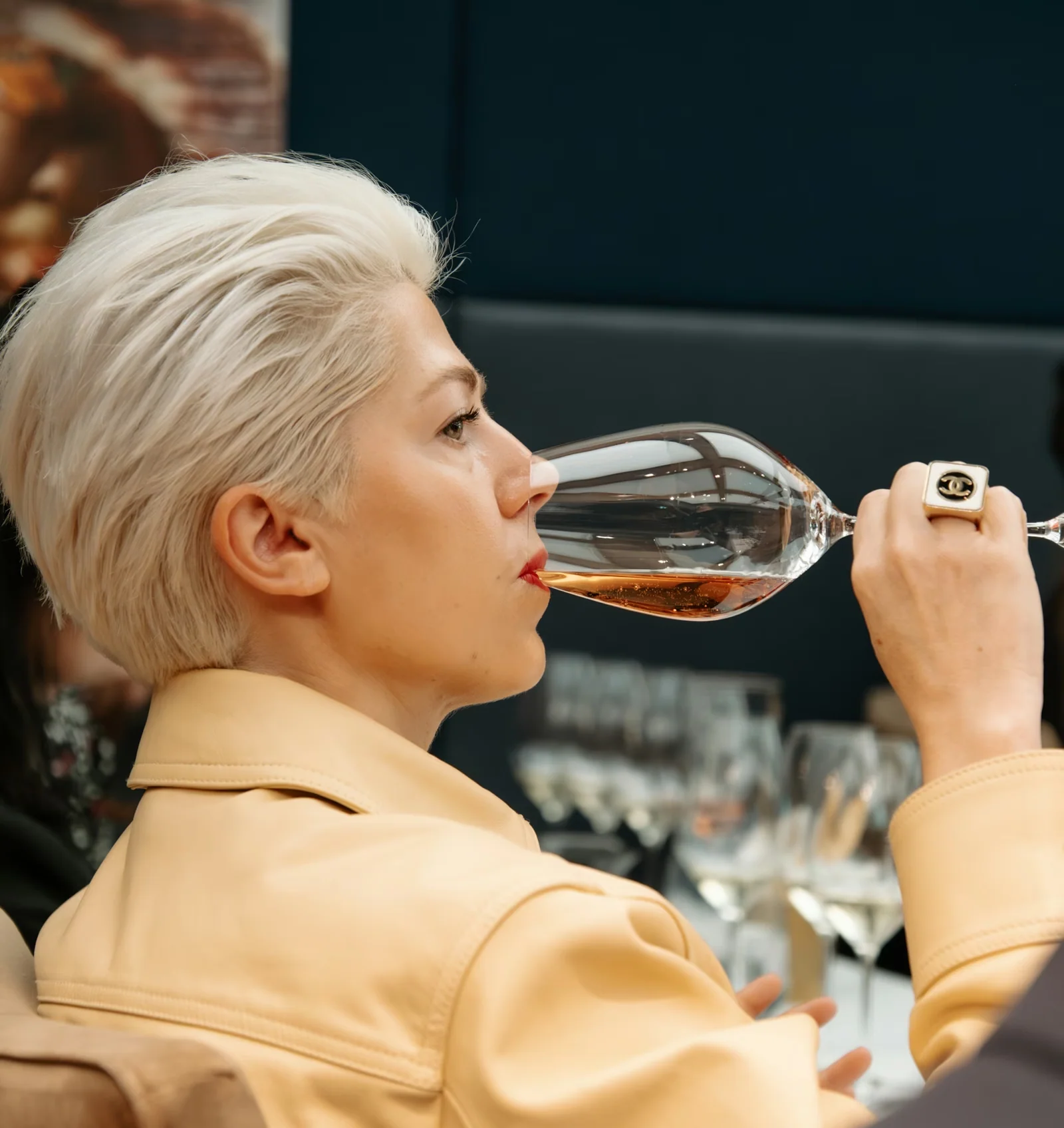 Person in a peach jacket tasting sparkling rosé from a large wine glass