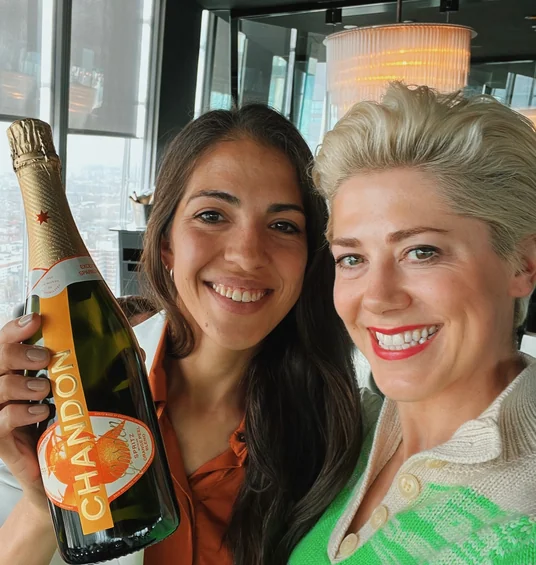 Two people smiling indoors beside a bottle of Chandon Garden Spritz