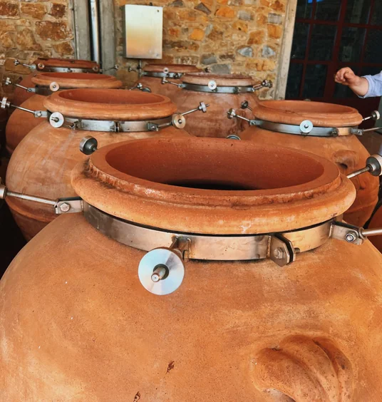 Large terracotta wine fermentation vessels with metal fittings inside a stone winery