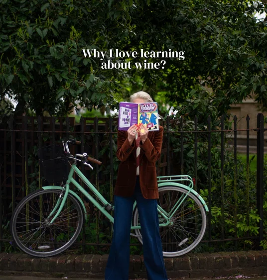 Person holding a magazine beside a mint-green bicycle under leafy trees