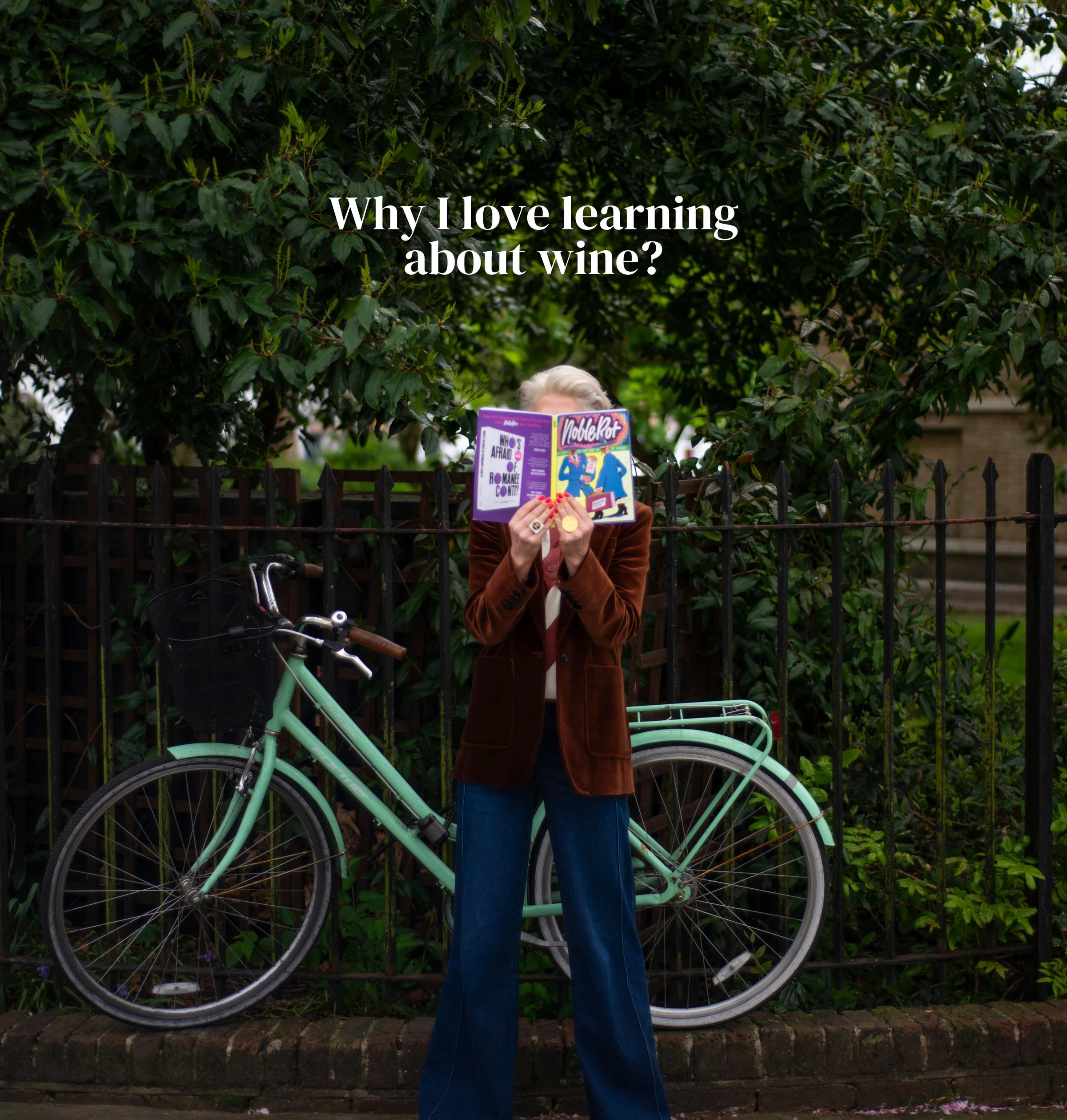 Person holding a magazine beside a mint-green bicycle under leafy trees
