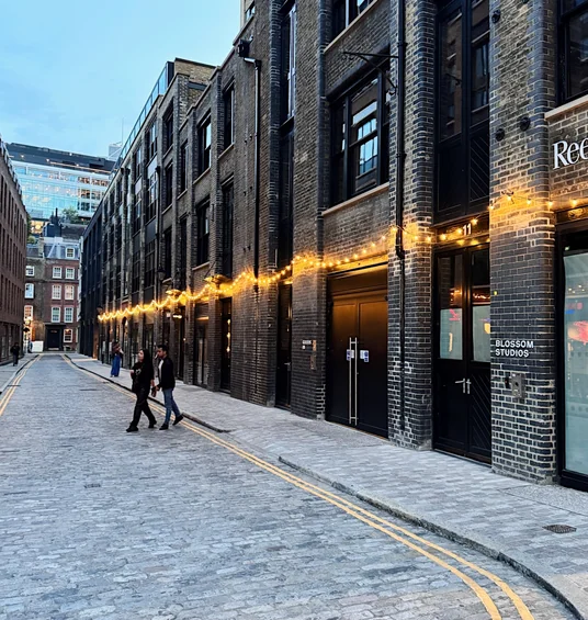 Cobblestoned London street with a brick venue lit by string lights