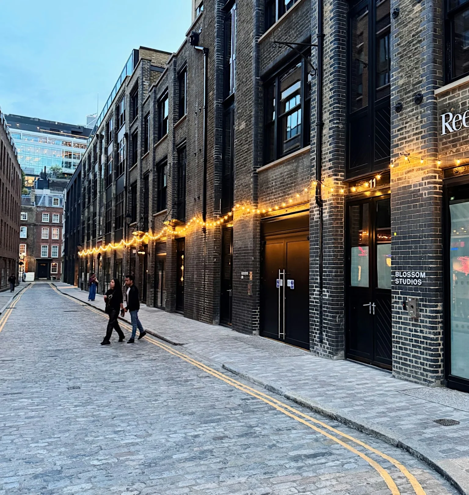 Cobblestoned London street with a brick venue lit by string lights