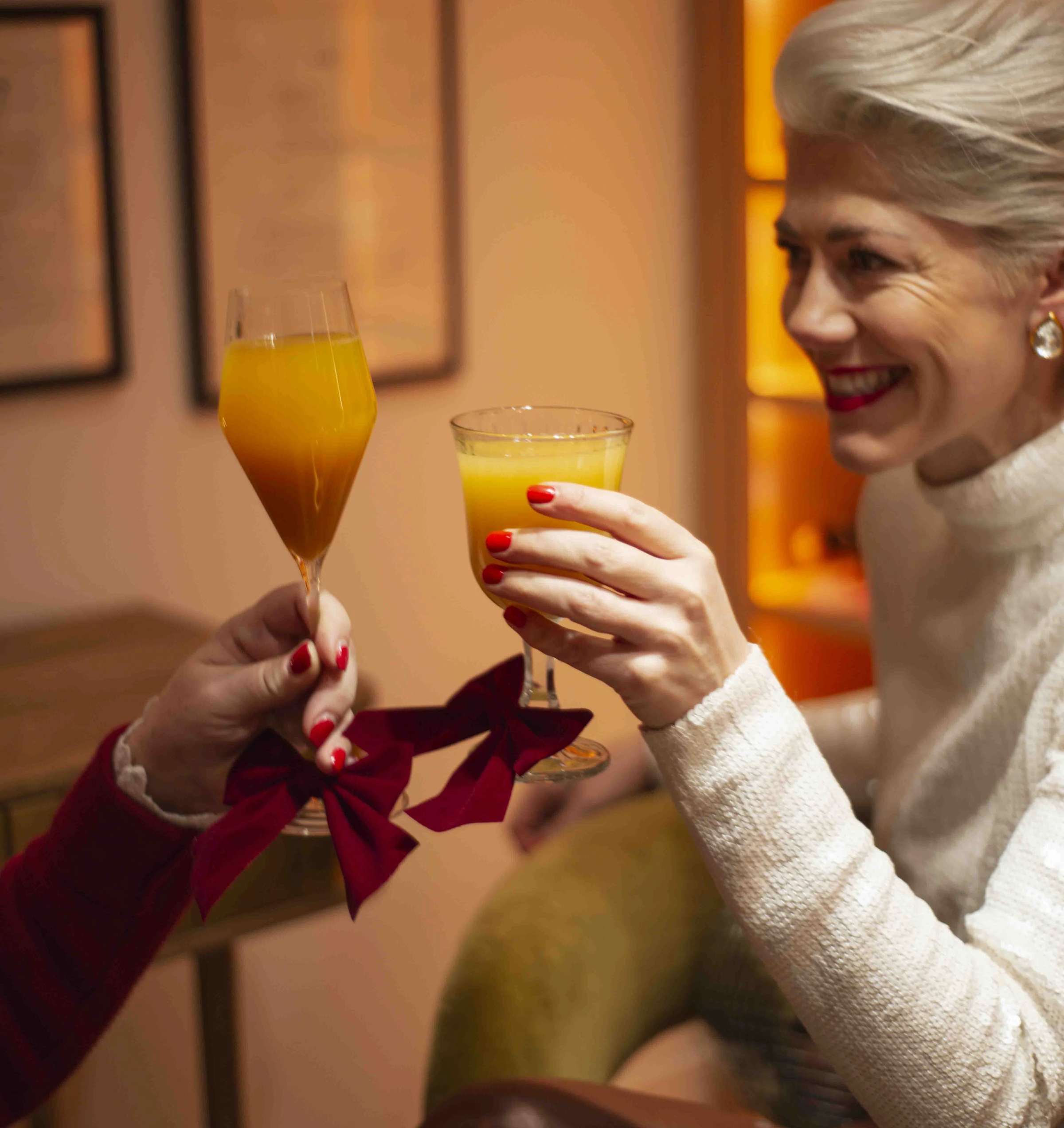 Two people raise orange prosecco cocktails in a warmly lit room