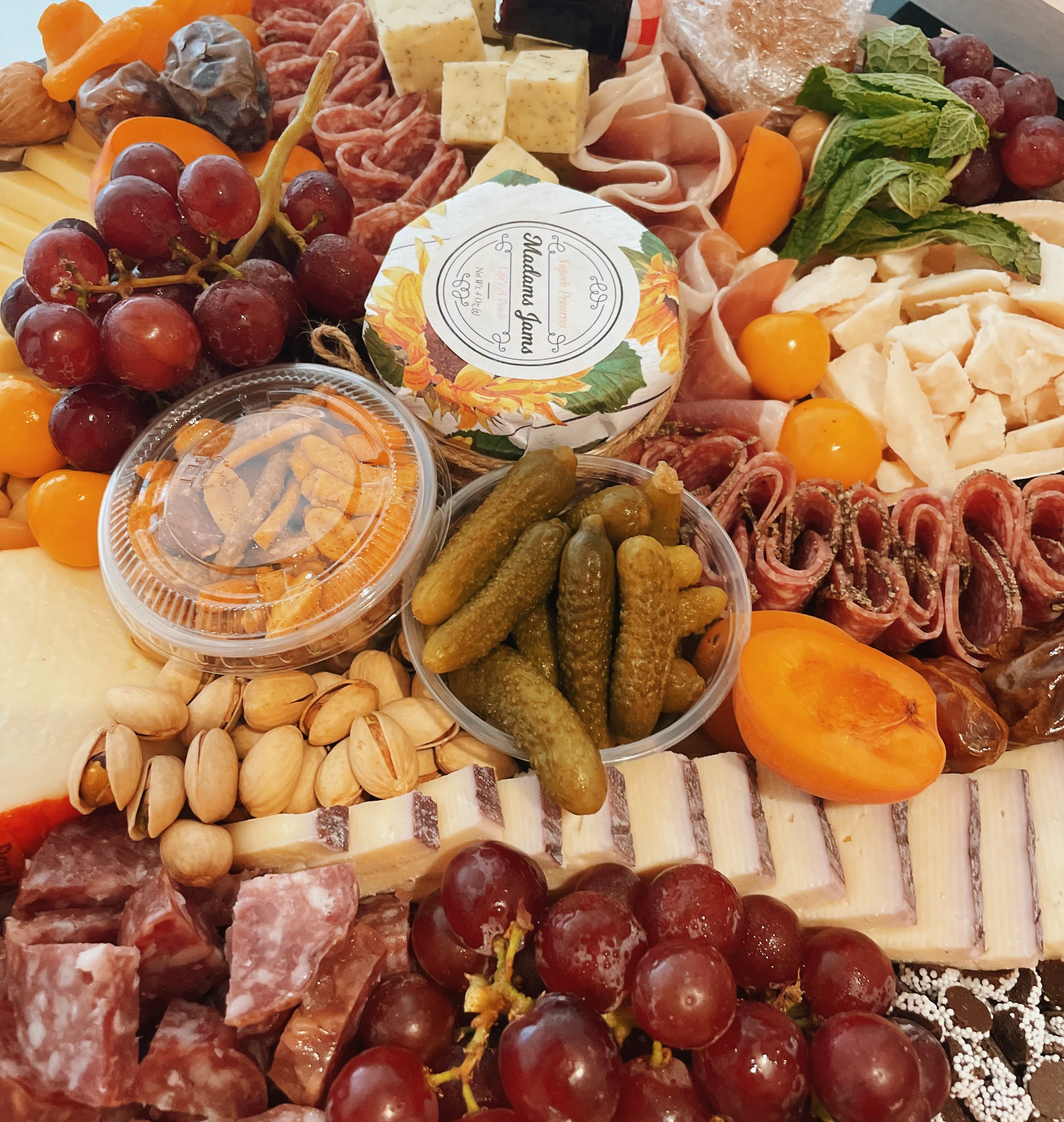 A richly arranged sharing board with cheeses, cured meats, grapes, pickles, fruit and crackers