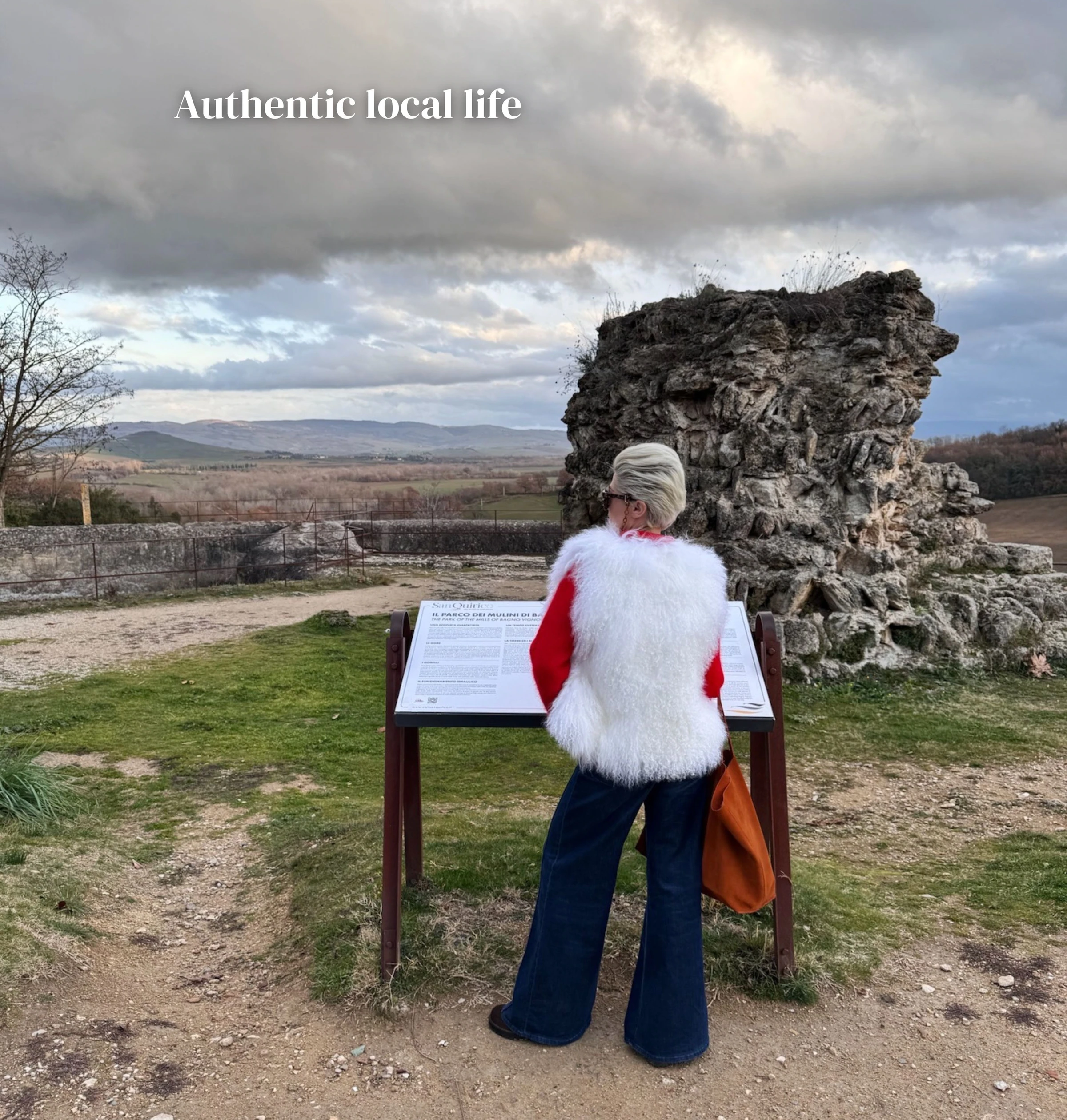 Visitor reading an information board beside a weathered stone ruin in the Tuscan countryside