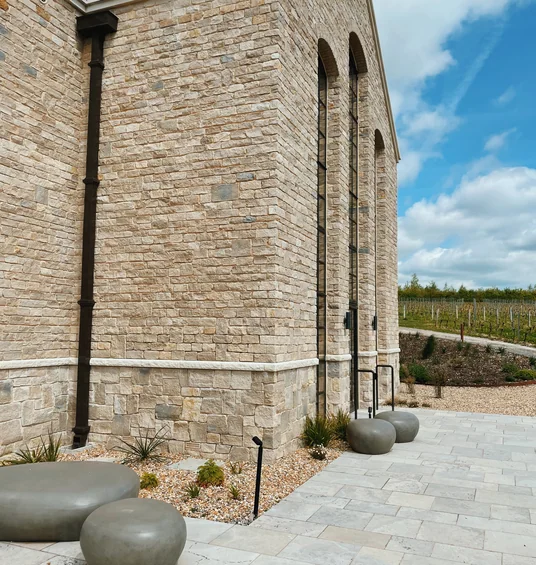 Exton Park's stone winery building beside a vineyard, with curved stone seats on a paved terrace